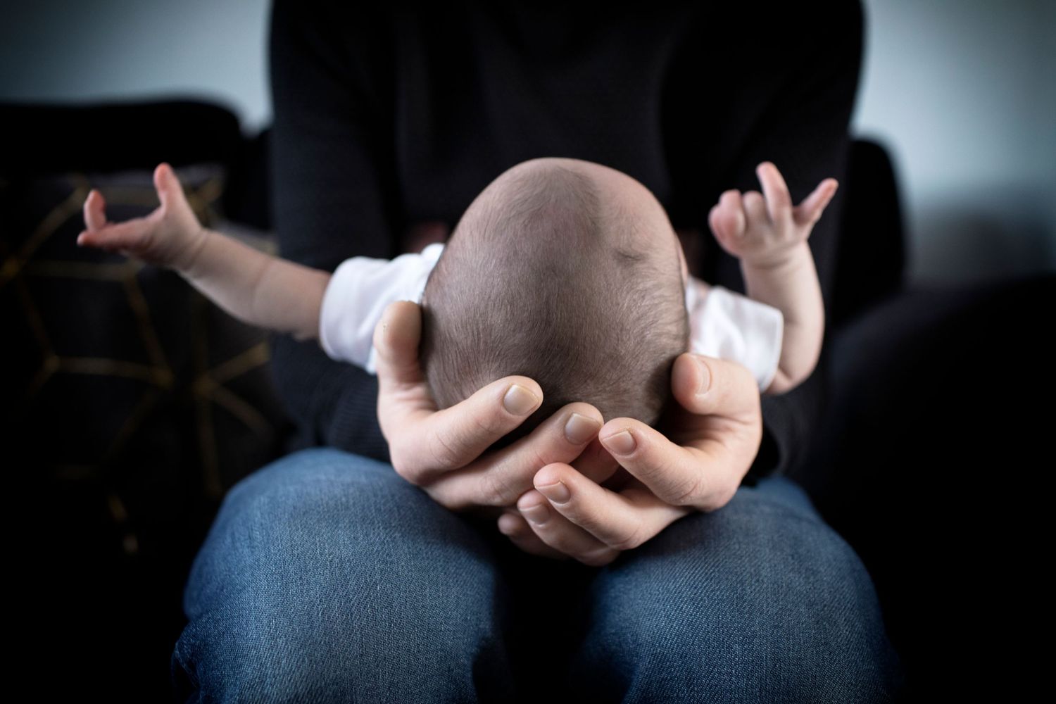 Candid shot of parent cradling newborn baby's head in their hands. Whitefield, UK