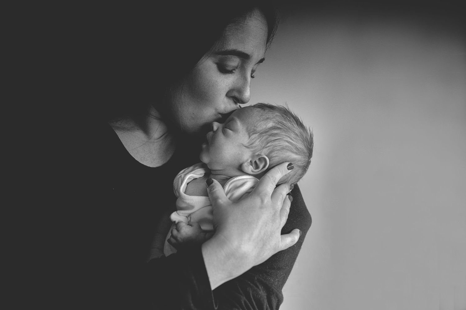 Mom gently kissing her newborn baby’s forehead, with a soft background in a Prestwich home