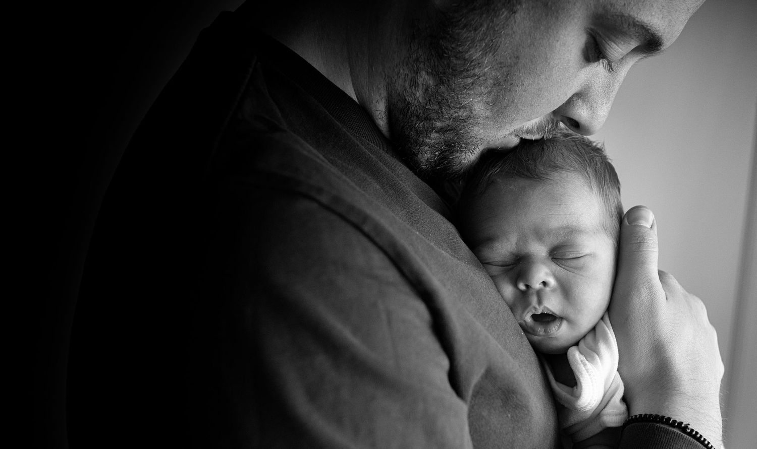 Father gently cradling his newborn in a serene and loving pose, captured in a home setting in Prestwich