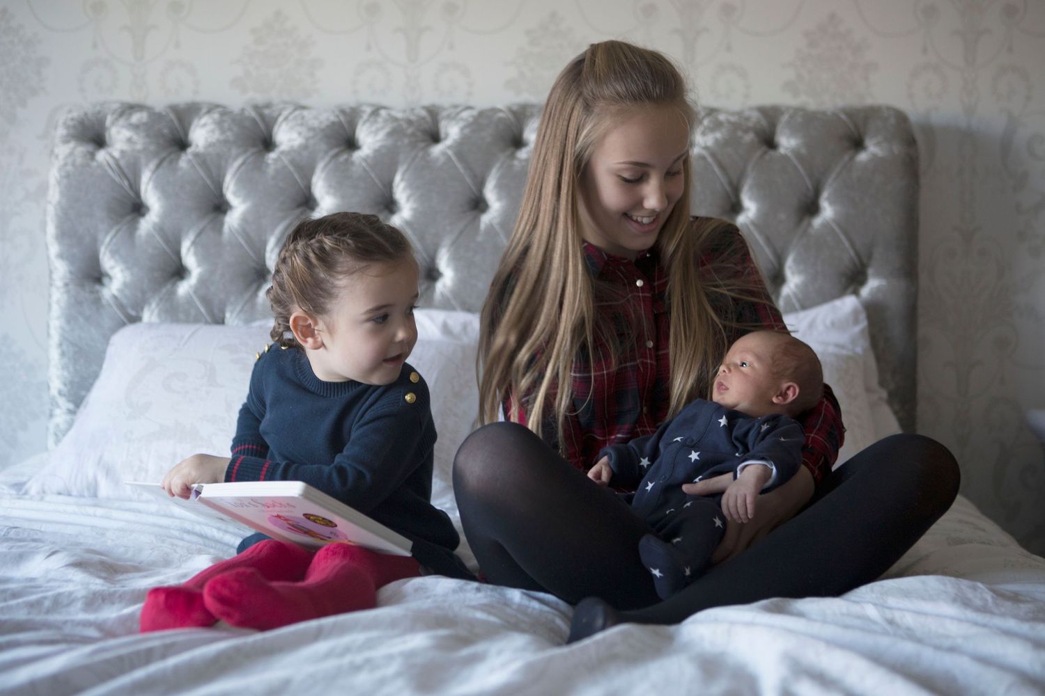 Family photography session in Whitefield, Manchester, with siblings reading a book and sharing a tender moment with their newborn sibling