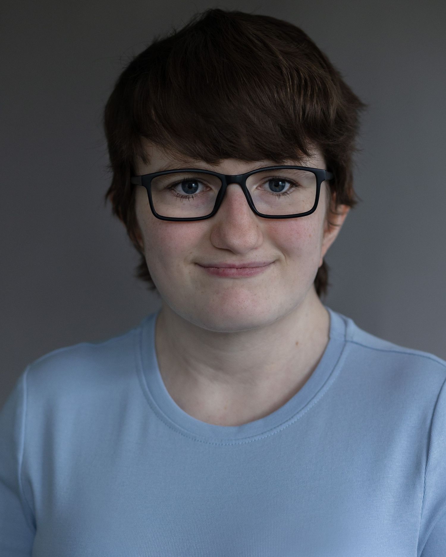 A young woman with short hair and glasses smiling for an acting headshot in Manchester, showcasing confidence and personality