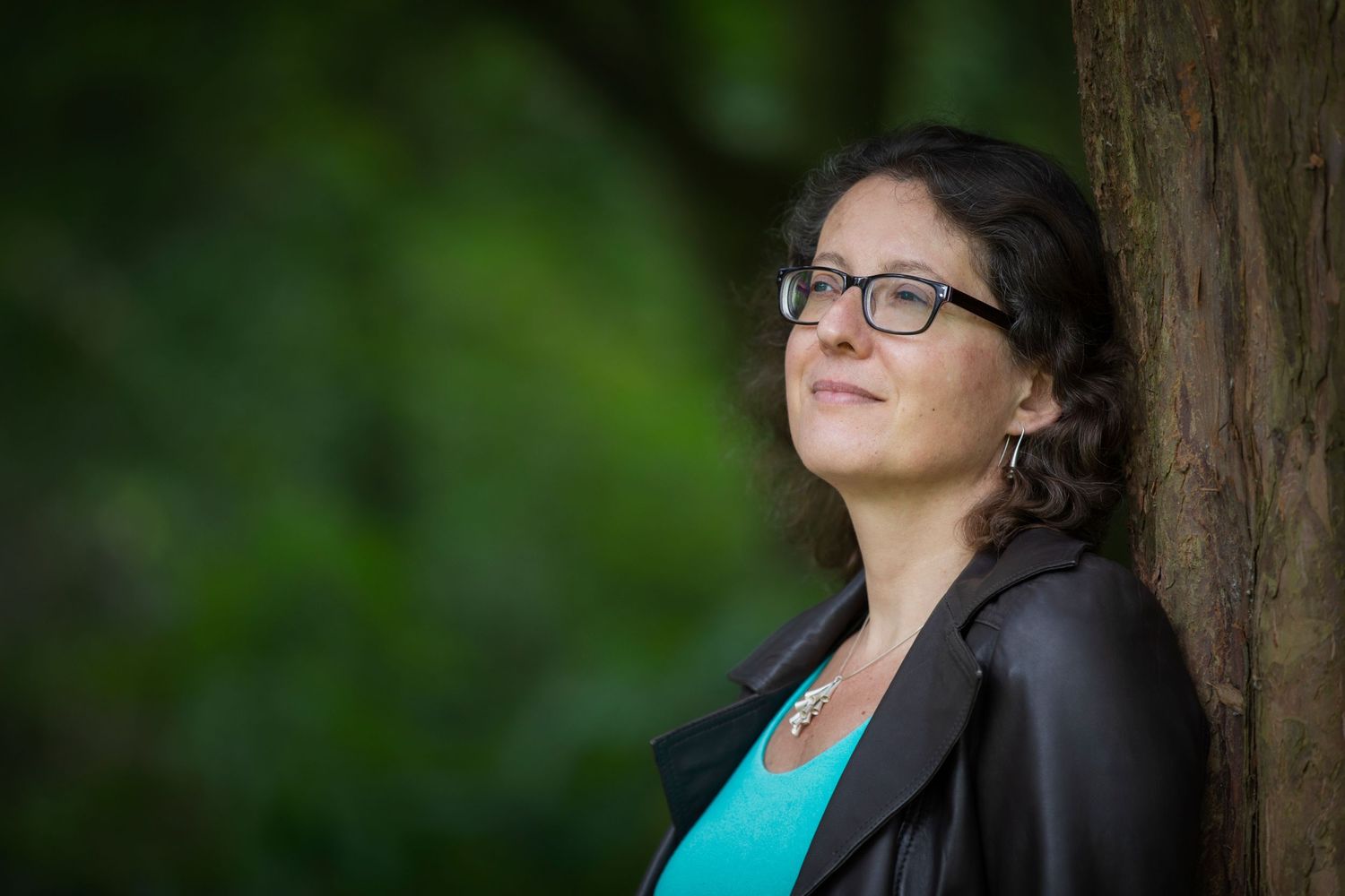 A woman leaning against a tree in a park in Whitefield, Manchester looking pensive during a personal branding session.