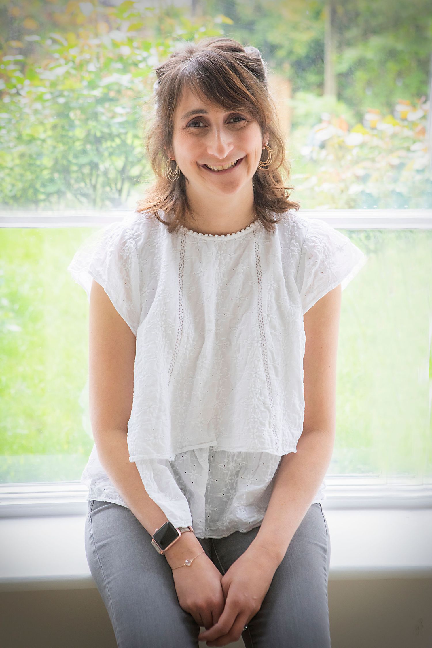 A woman sitting by the window in her home in Prestwich, smiling warmly at the camera during a personal branding photo session.