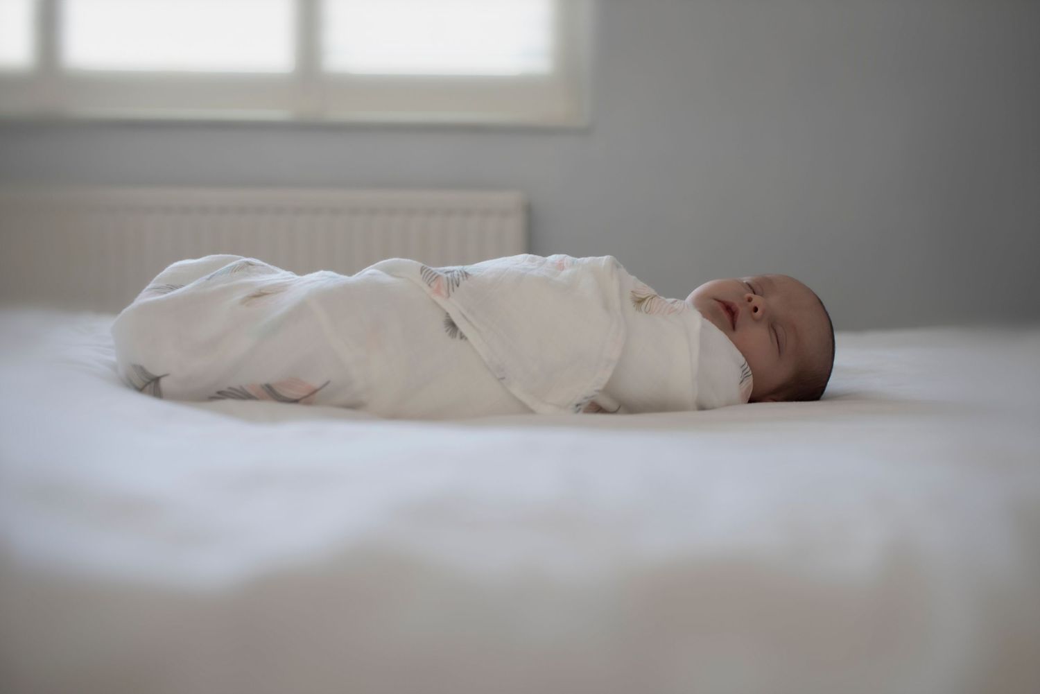 A newborn baby sleeps peacefully on a bed, wrapped up in a soft blanket. Manchester, UK
