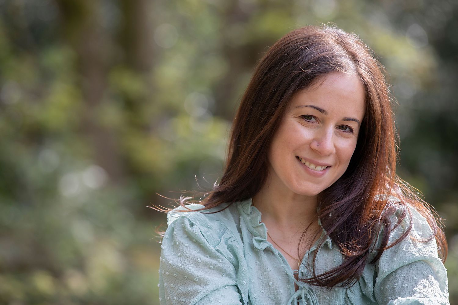 A woman smiling at the camera in a park during a personal branding photo session in Whitefield, exuding confidence and warmth.