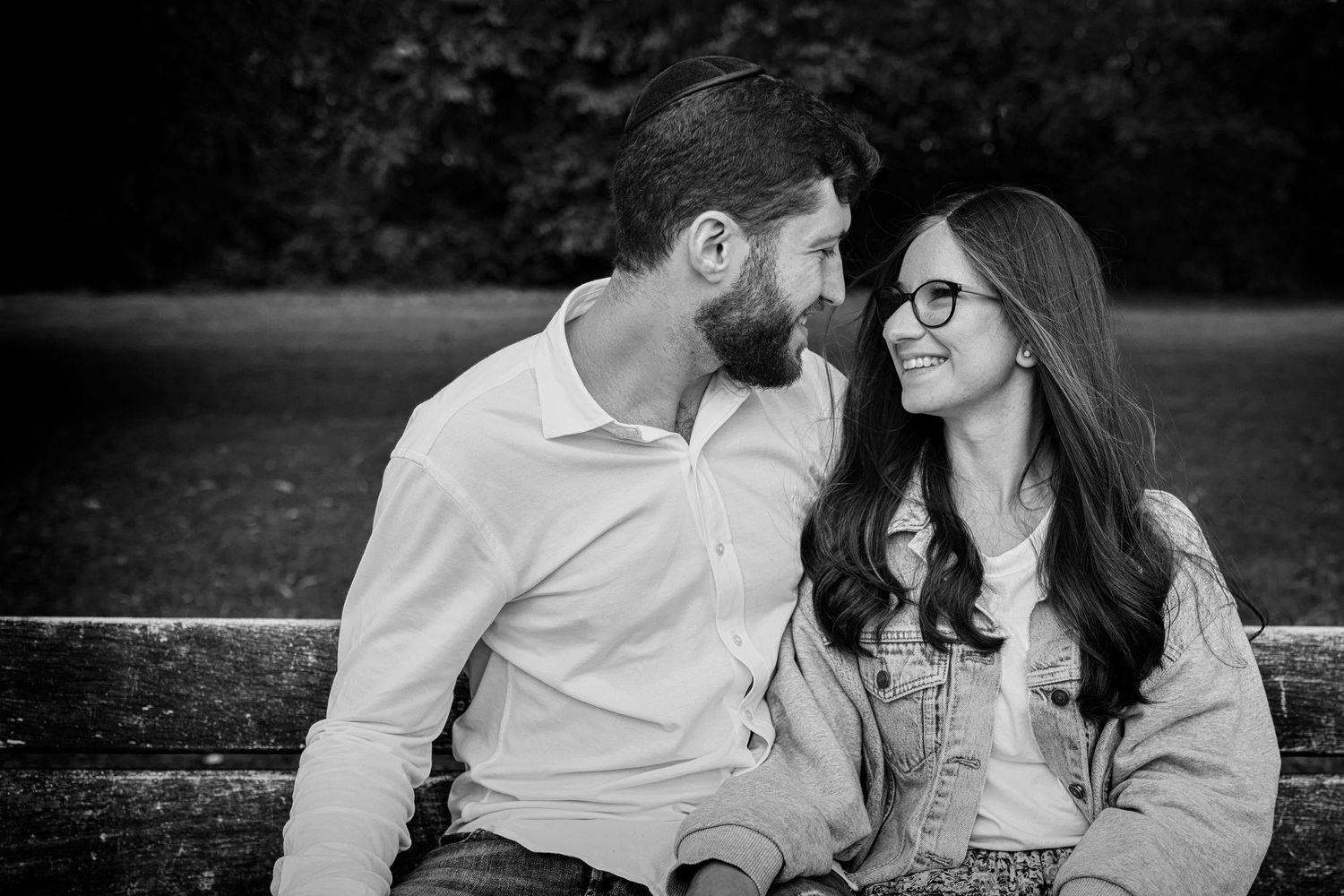 Candid black and white family photo of a couple looking lovingly into each others eyes sitting on a bench at a local park in Manchester.