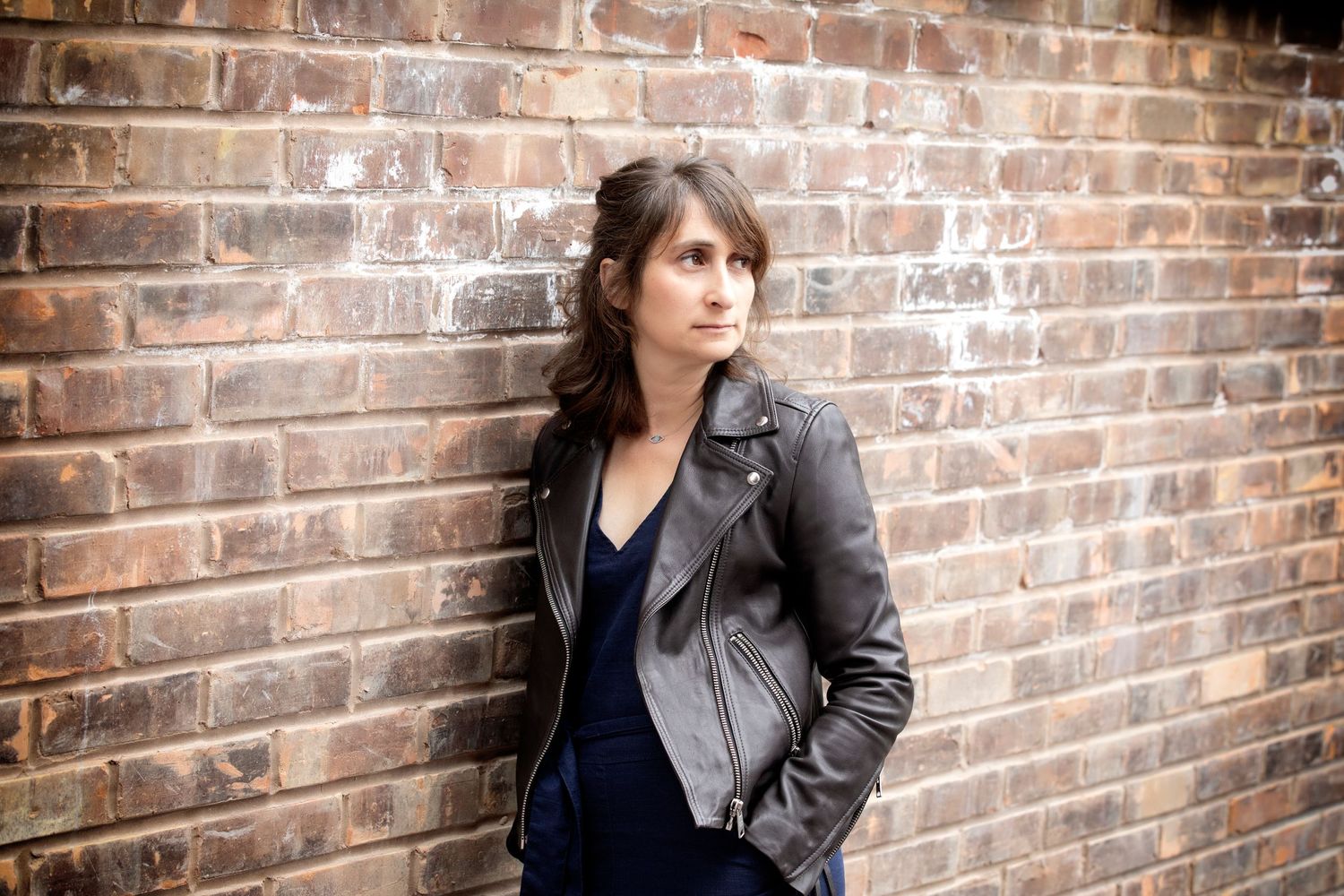 A woman leaning against a brick wall in her home in Prestwich, exuding confidence and style during a personal branding photo session