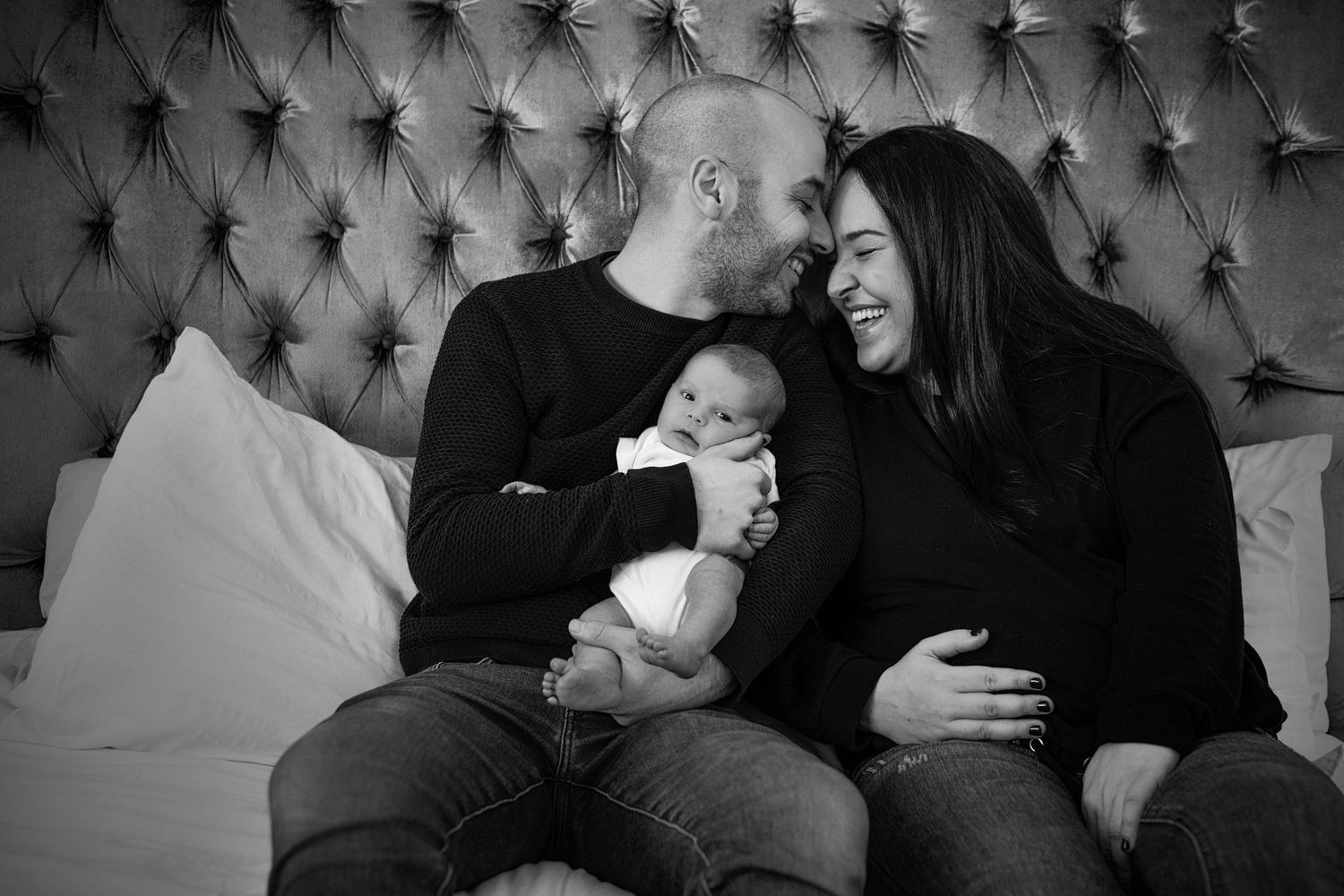 A mum and dad laugh together as they lovingly cradle their newborn baby in their bedroom in their Manchester home. UK