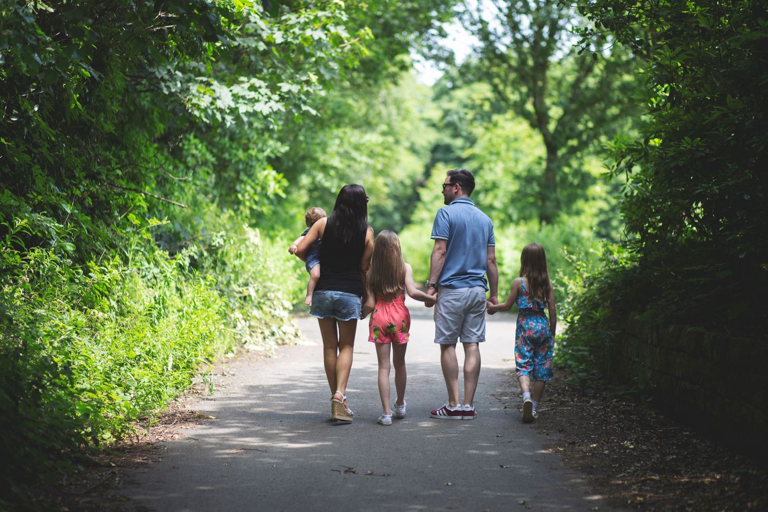 Candid photograph of a family of five walking together in a beautiful park during the summer in Whitefield, Manchester.
