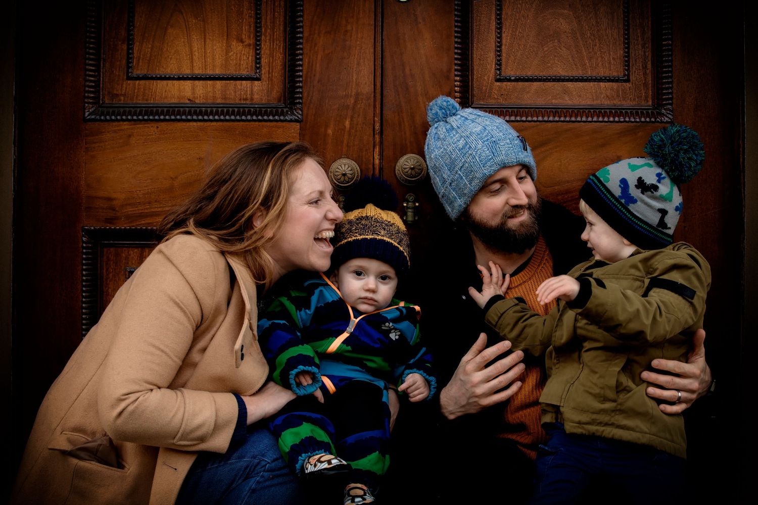 Beautiful family portrait with two children and their parents, huddled together outdoors in a park in Manchester