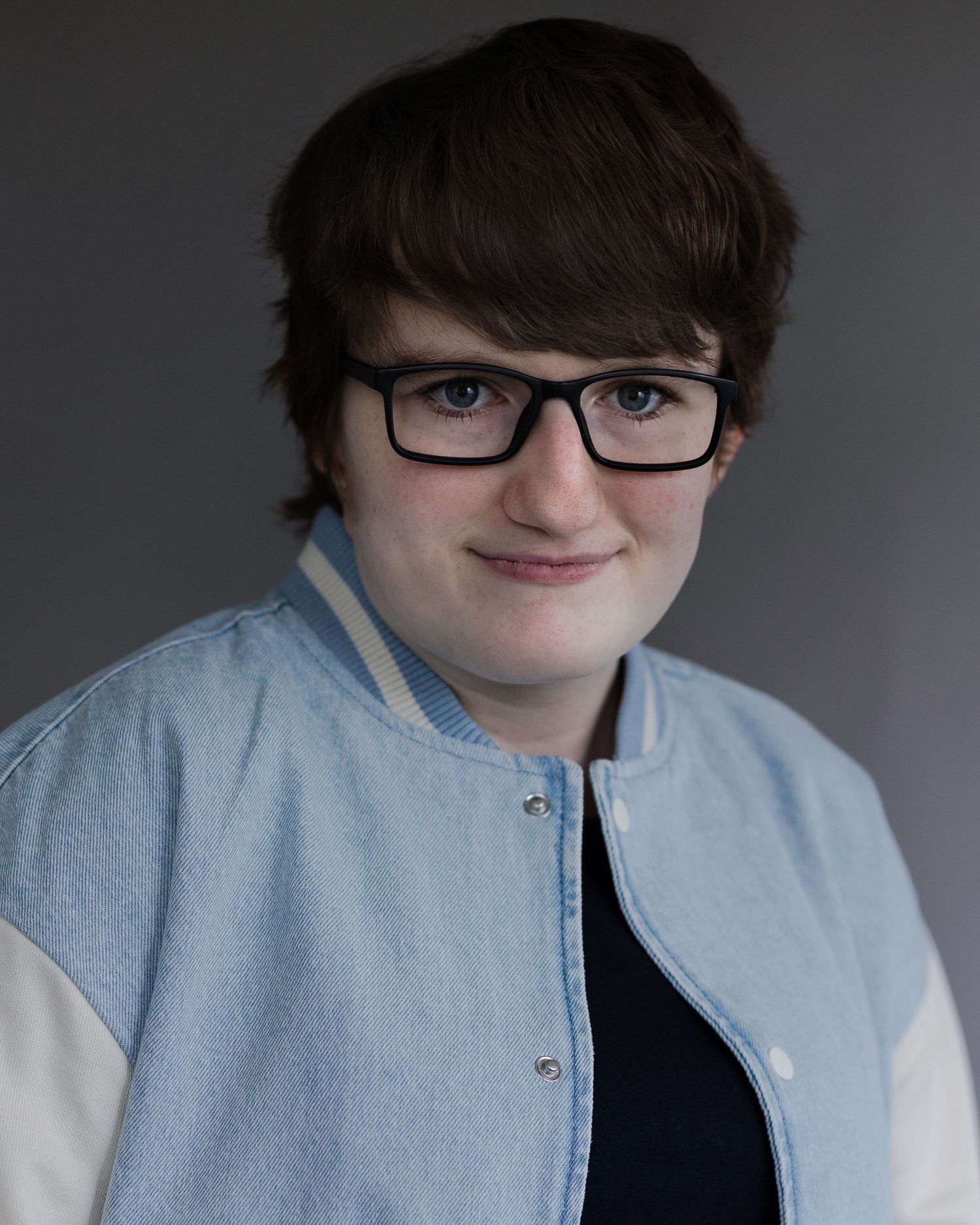 Young woman with short hair and glasses smiling for an acting headshot in Manchester, displaying confidence during a headshot session