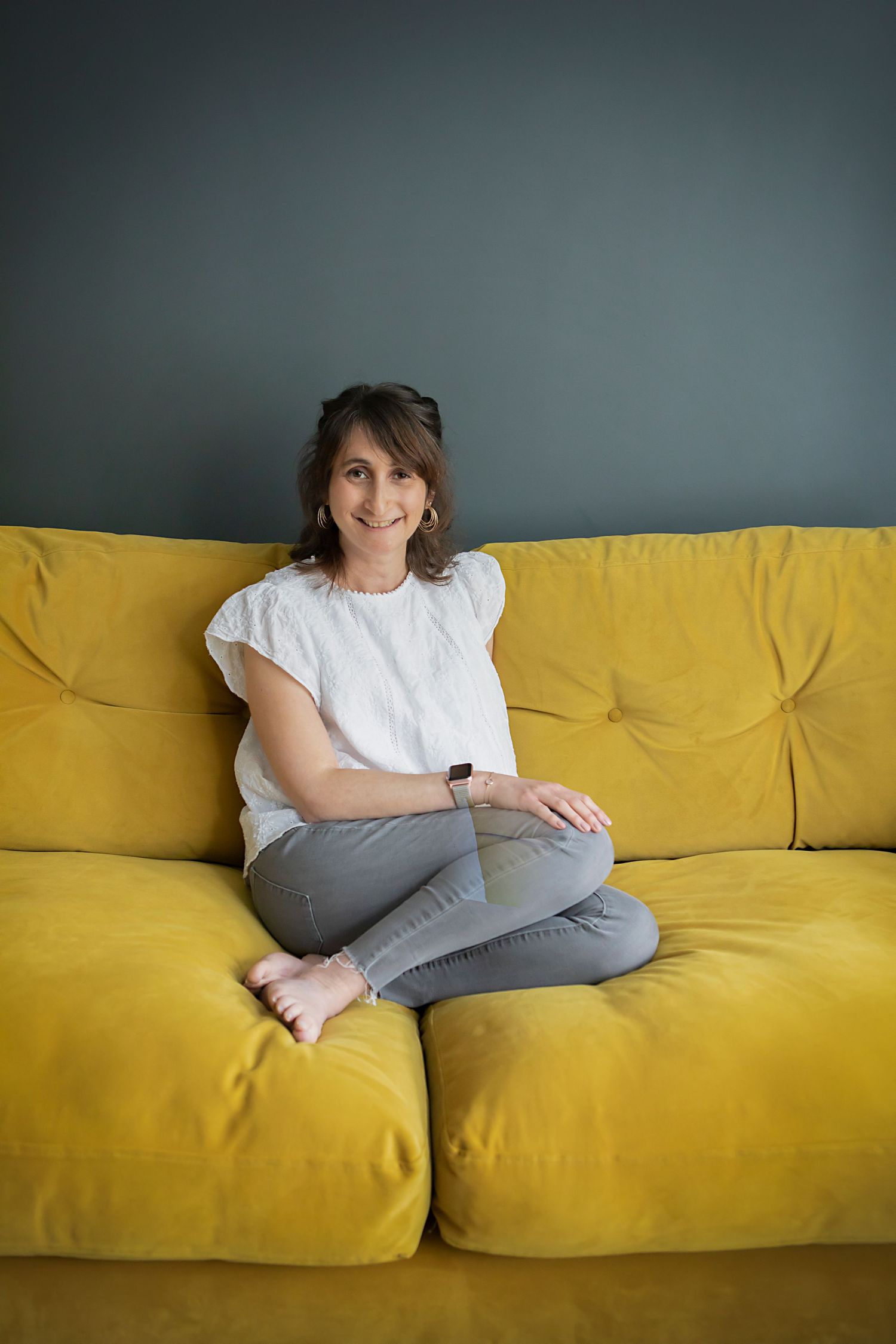 A woman sitting on a bright yellow sofa in her home in Prestwich, looking relaxed and confident during a personal branding photo session.