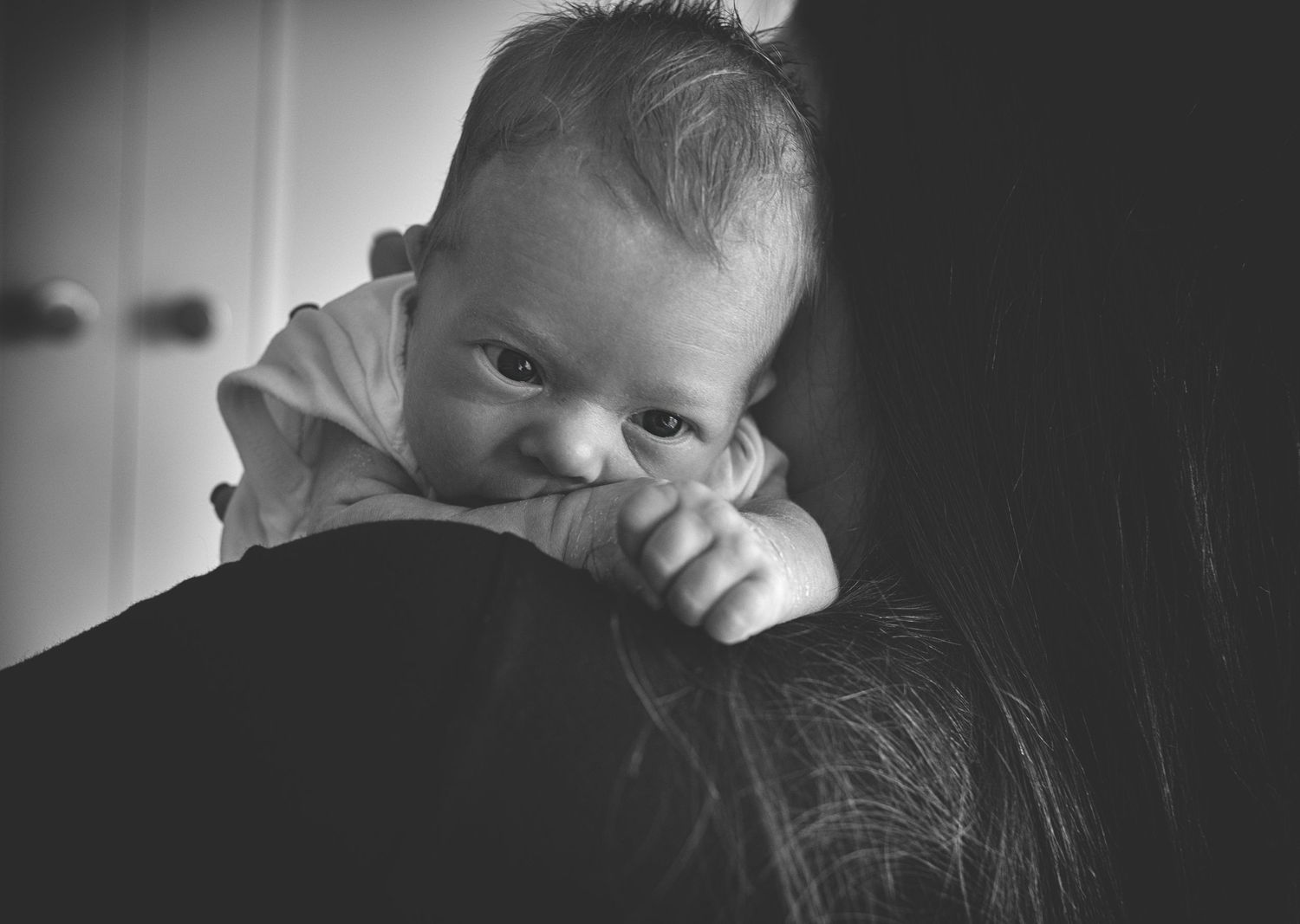 Tender moment between a mother and her newborn baby with baby looking over mum's shoulder in the family home in Prestwich