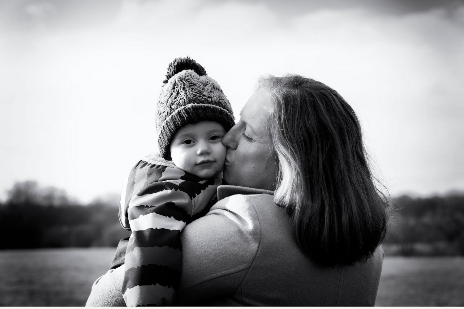 Black and white photo showing a tender moment as mum kisses her son on the cheek in an outdoor setting in Prestwich, Greater Manchester