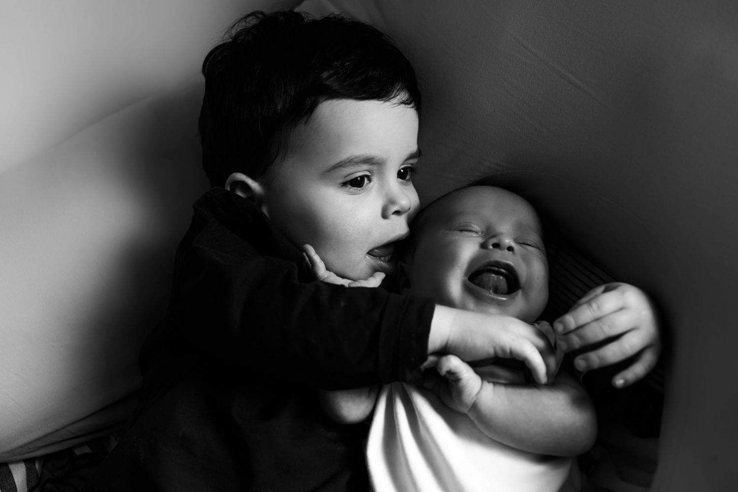 Candid black and white photograph of siibling bonding with a newborn brother in their family home in Prestwich, Manchester.