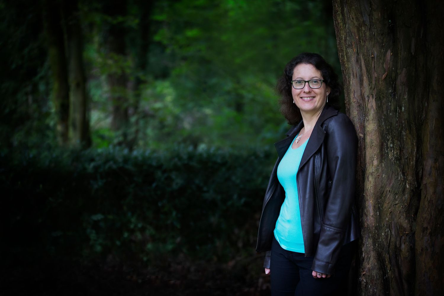 A woman leaning against a tree in a park in Whitefield, exuding confidence and relaxation during a personal branding session