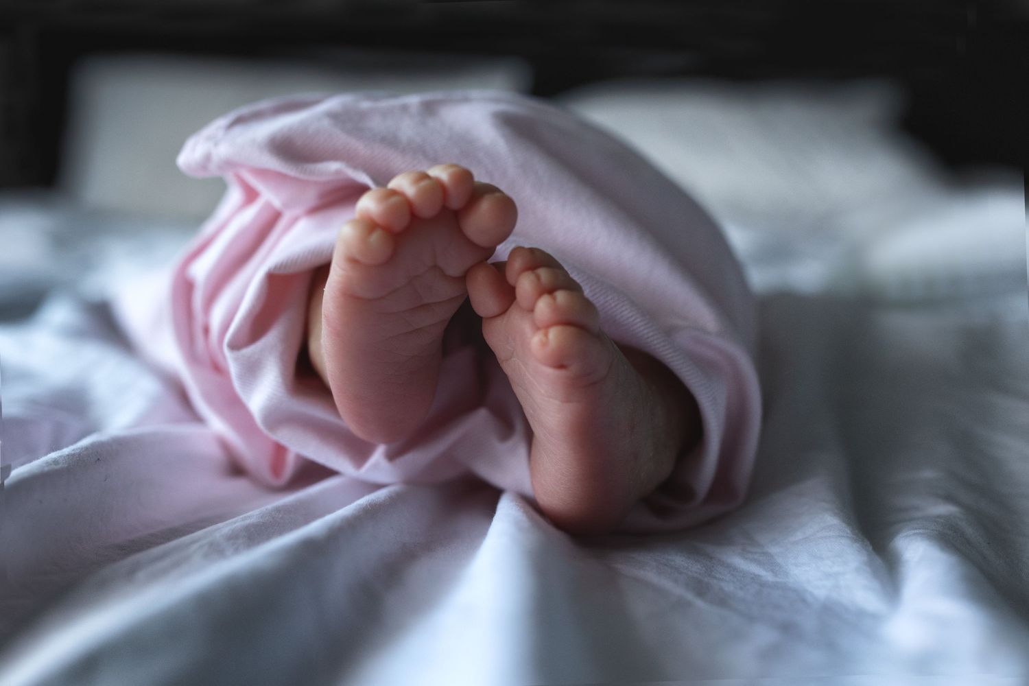 Close-up of a newborn’s tiny feet wrapped up in soft pink blanket. Manchester, UK