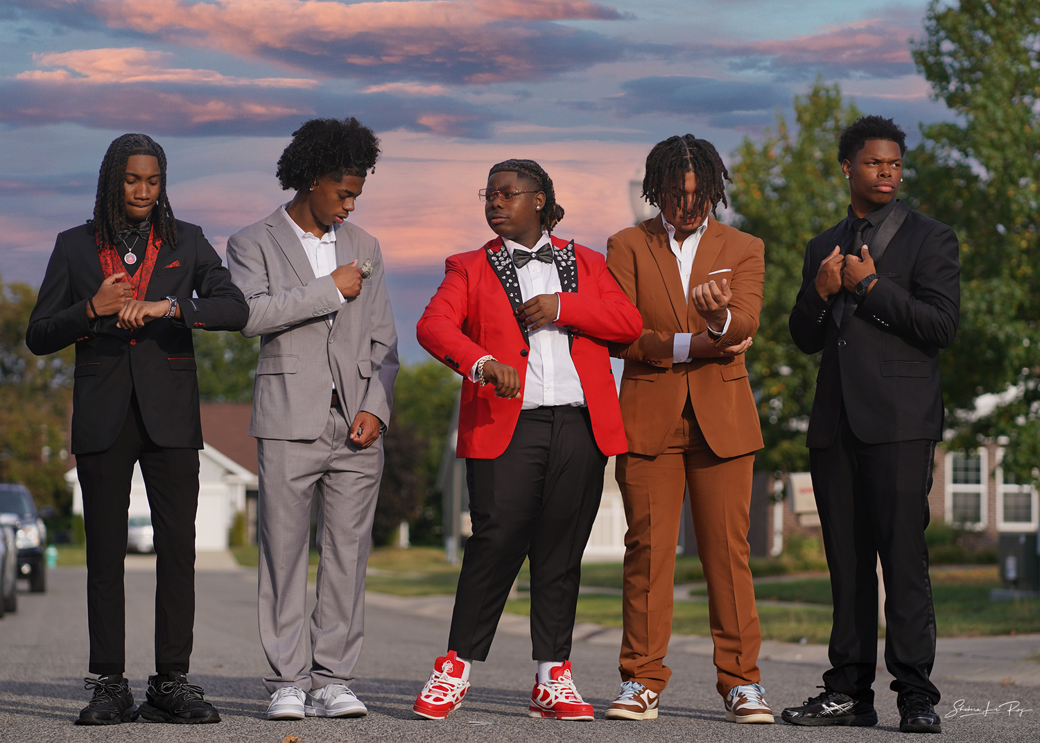 Group of people showing off their colorful sneakers and shoes while standing in a line outdoors at sunset.