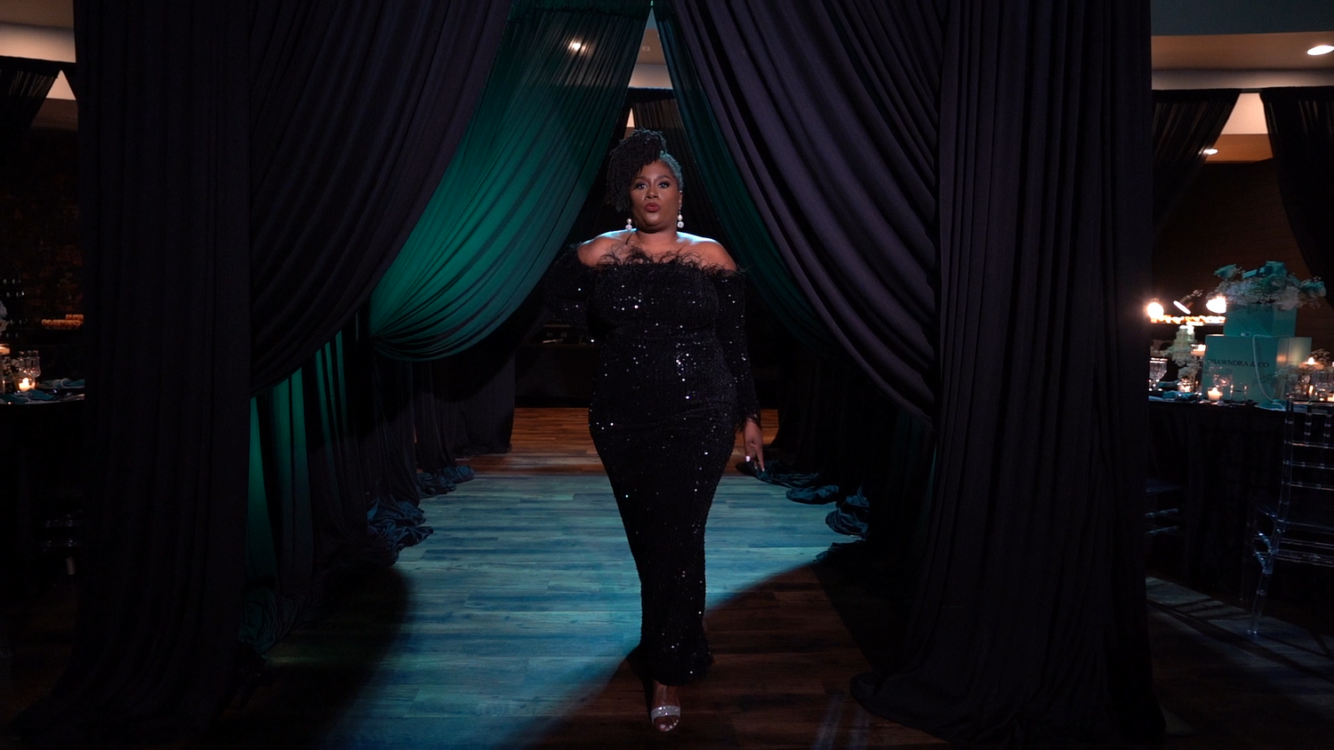 Person walks through dramatic curtained entrance wearing formal attire in moody lighting.