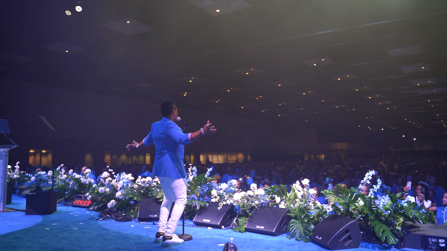 Stage performer in blue outfit entertaining audience in dimly lit venue.
