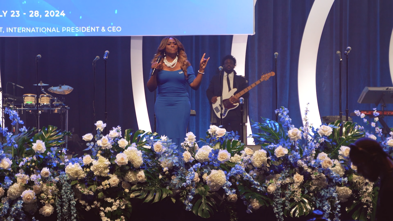 Performance on stage with elaborate blue and white floral arrangements.