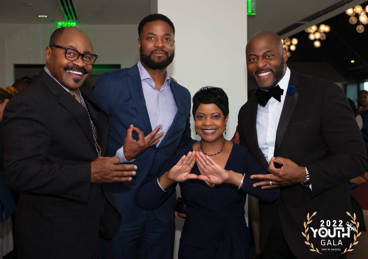 Four people in formal attire pose together and gesture at an elegant evening event.