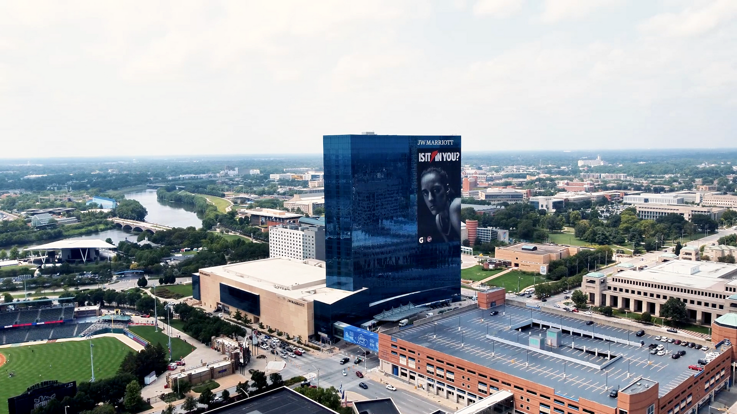 Aerial view of a modern blue glass building next to a sports stadium complex.