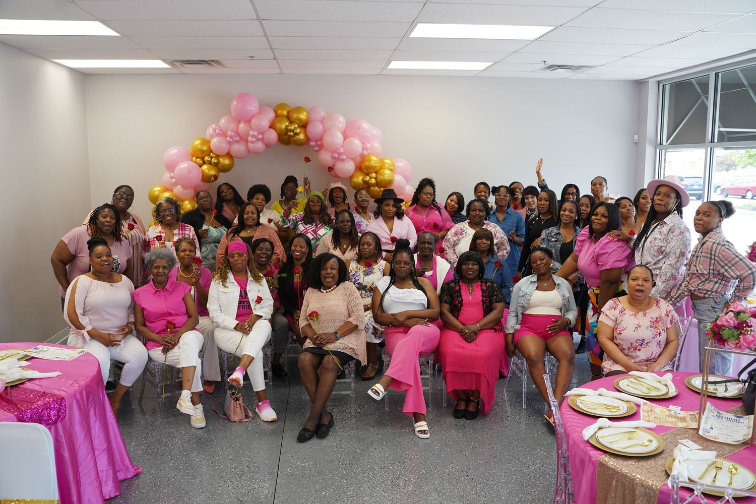 A large group gathered for a celebration with pink and gold balloon decorations.