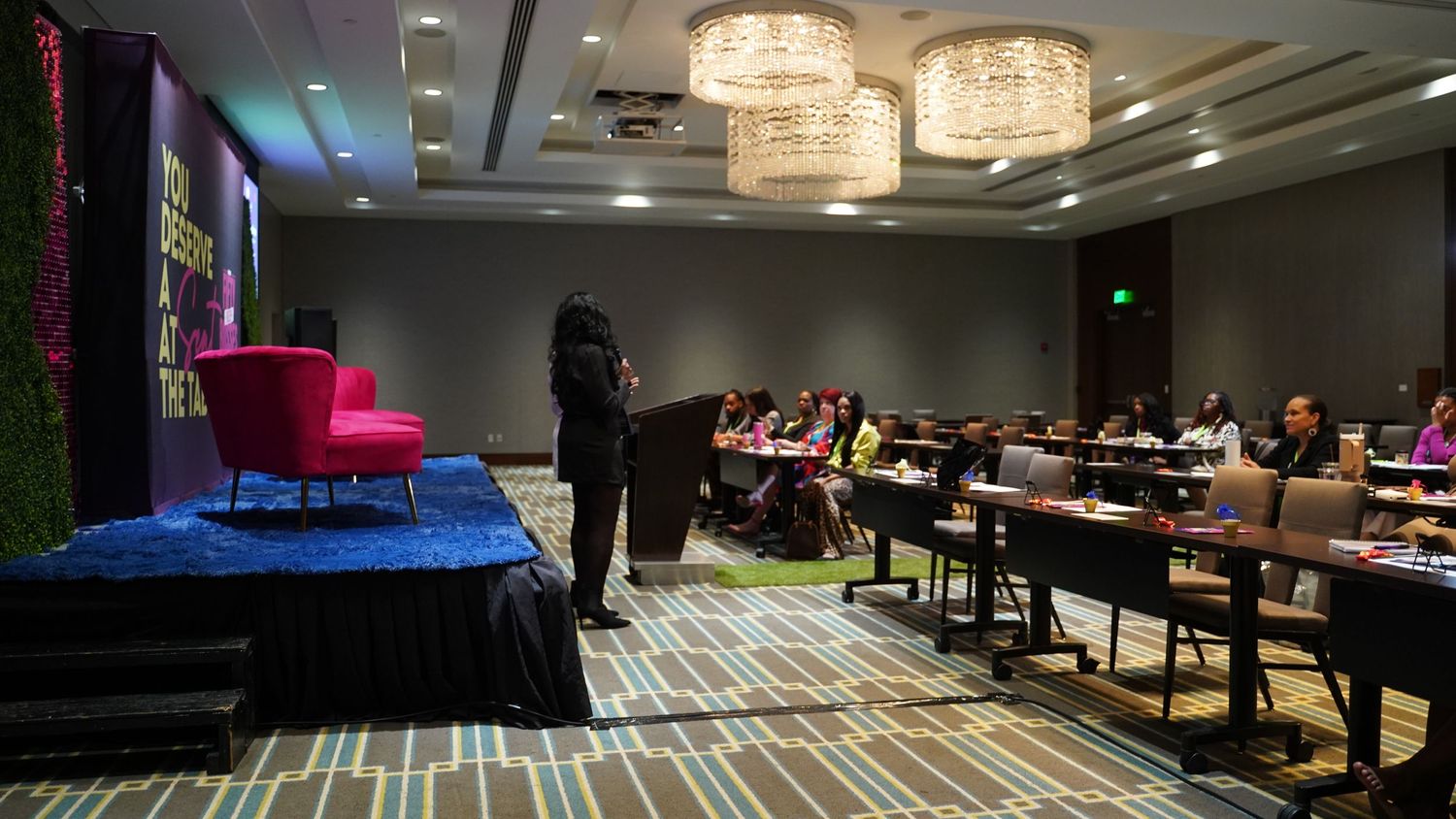 Empty conference room setup with presentation stage and theater-style seating under crystal chandeliers.