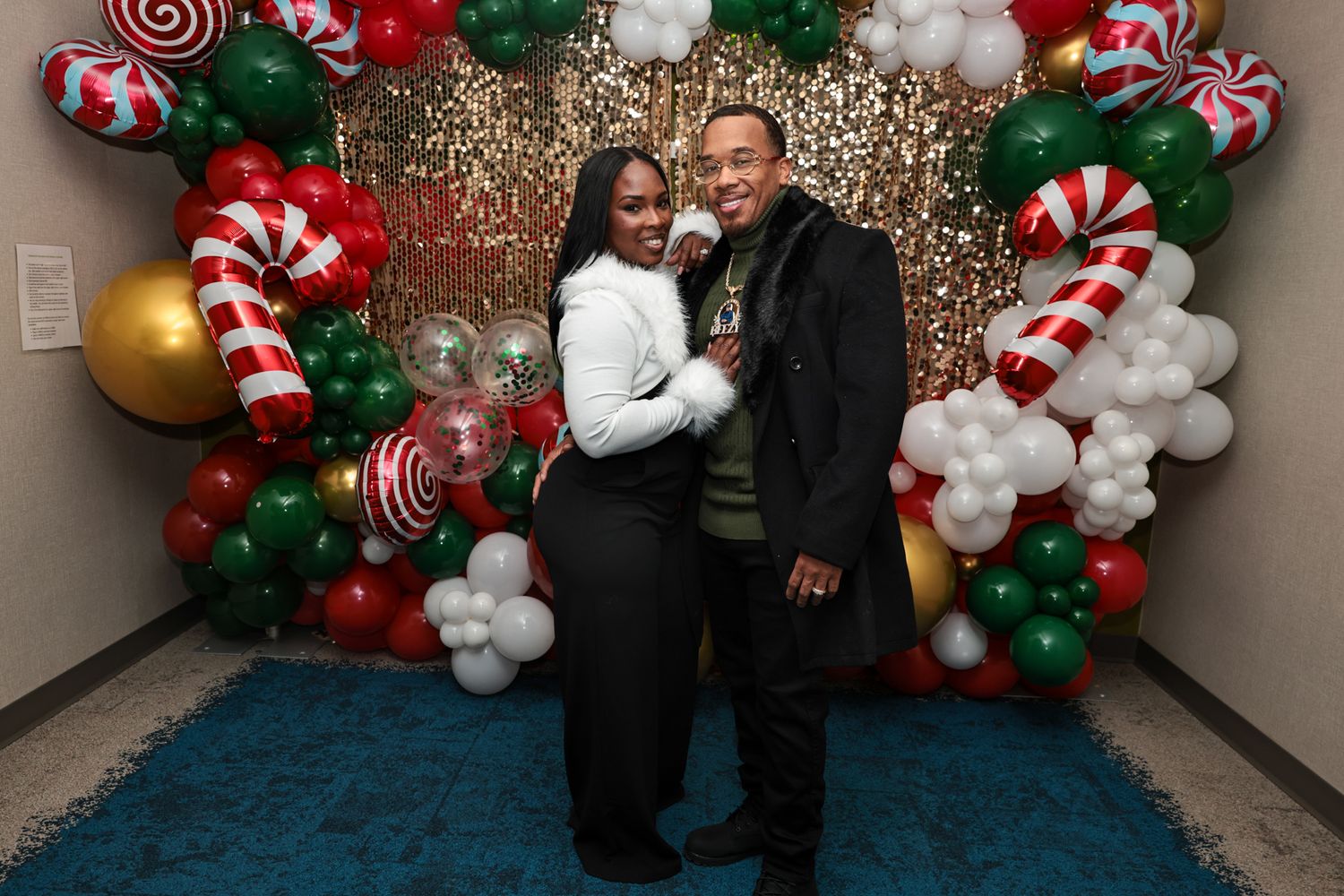 A festive holiday photo featuring a backdrop with candy cane decorations, ornaments, and balloon arrangements.