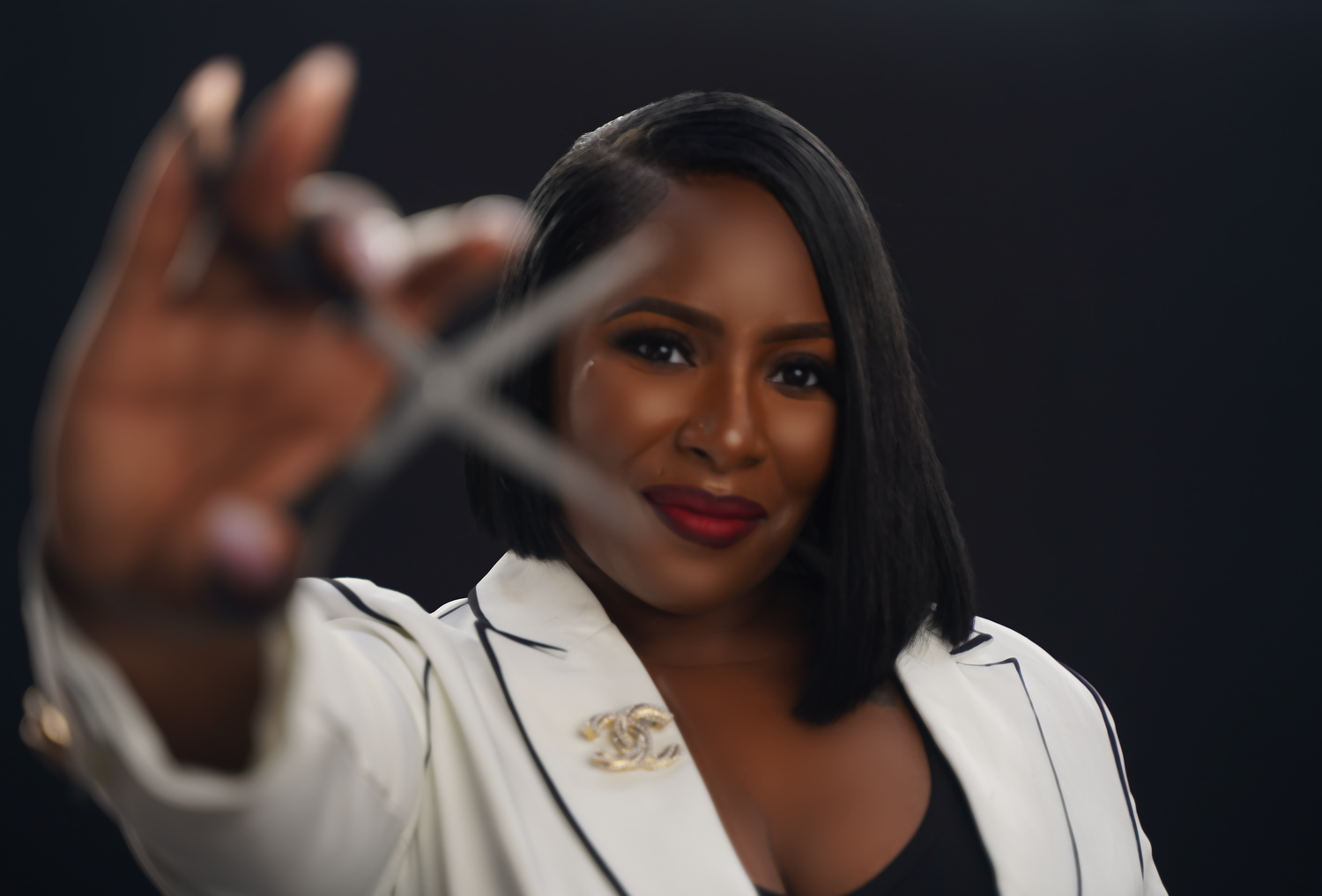 Studio portrait of professional in white blazer reaching toward camera on dark background.