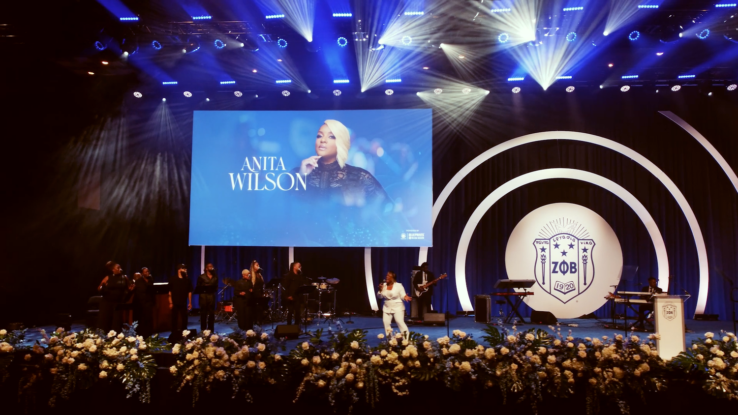 Concert stage with elegant floral decorations and large screen display during performance.