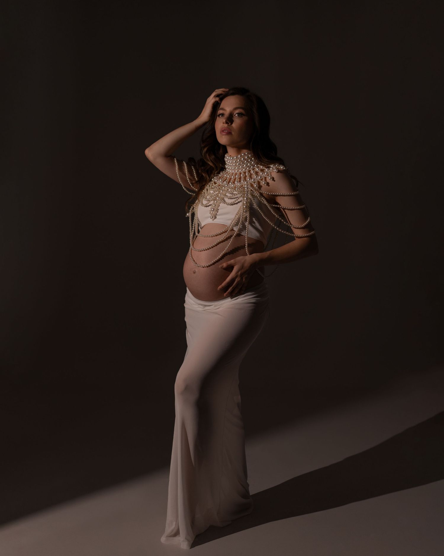 Mother-to-be in a dreamy, ethereal maternity session wearing white long skirt and top and pearl body chain.