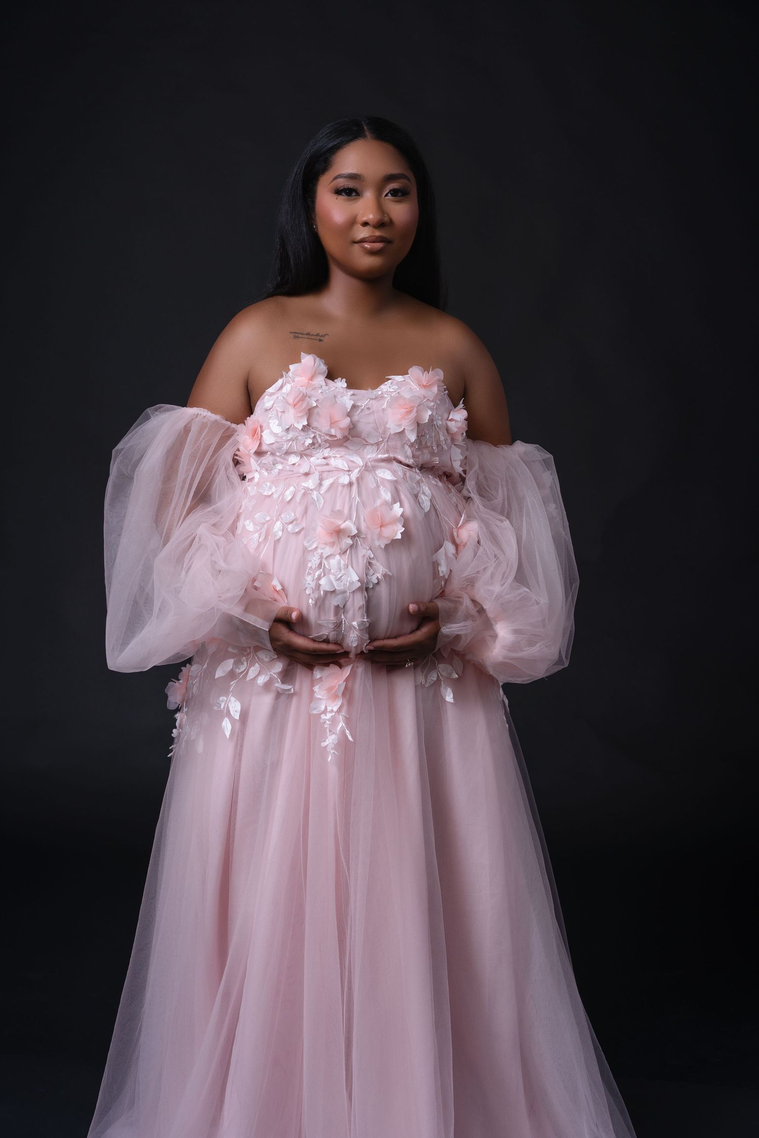 Pregnant woman in a pink long dress with flowers posing during a maternity photoshoot in Chicago. Her hair is dark.