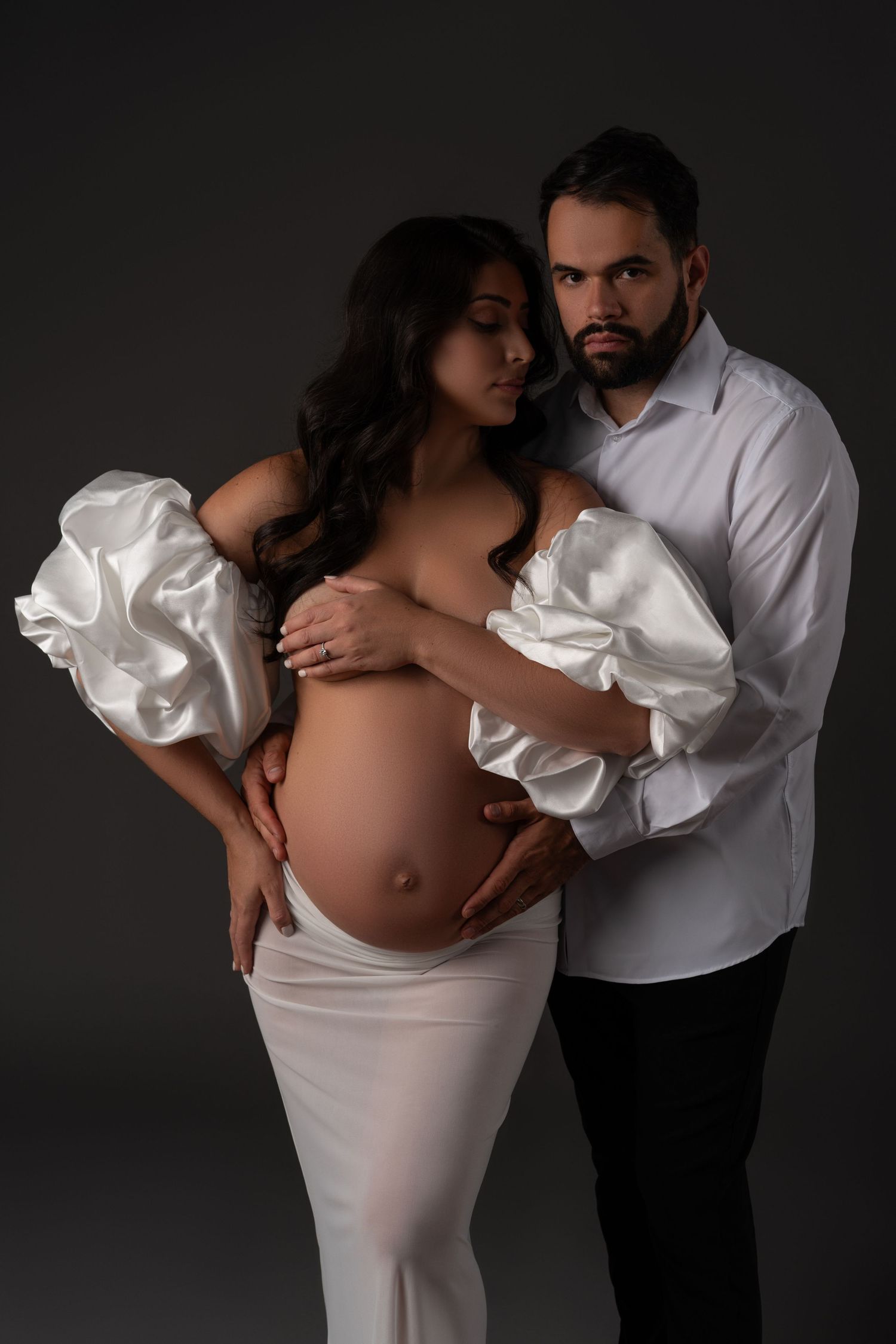 Maternity photoshoot in a Chicago— couple in elegant matching outfits, mom-to-be topless in a satin wrap and skirt, partner in white shirt.