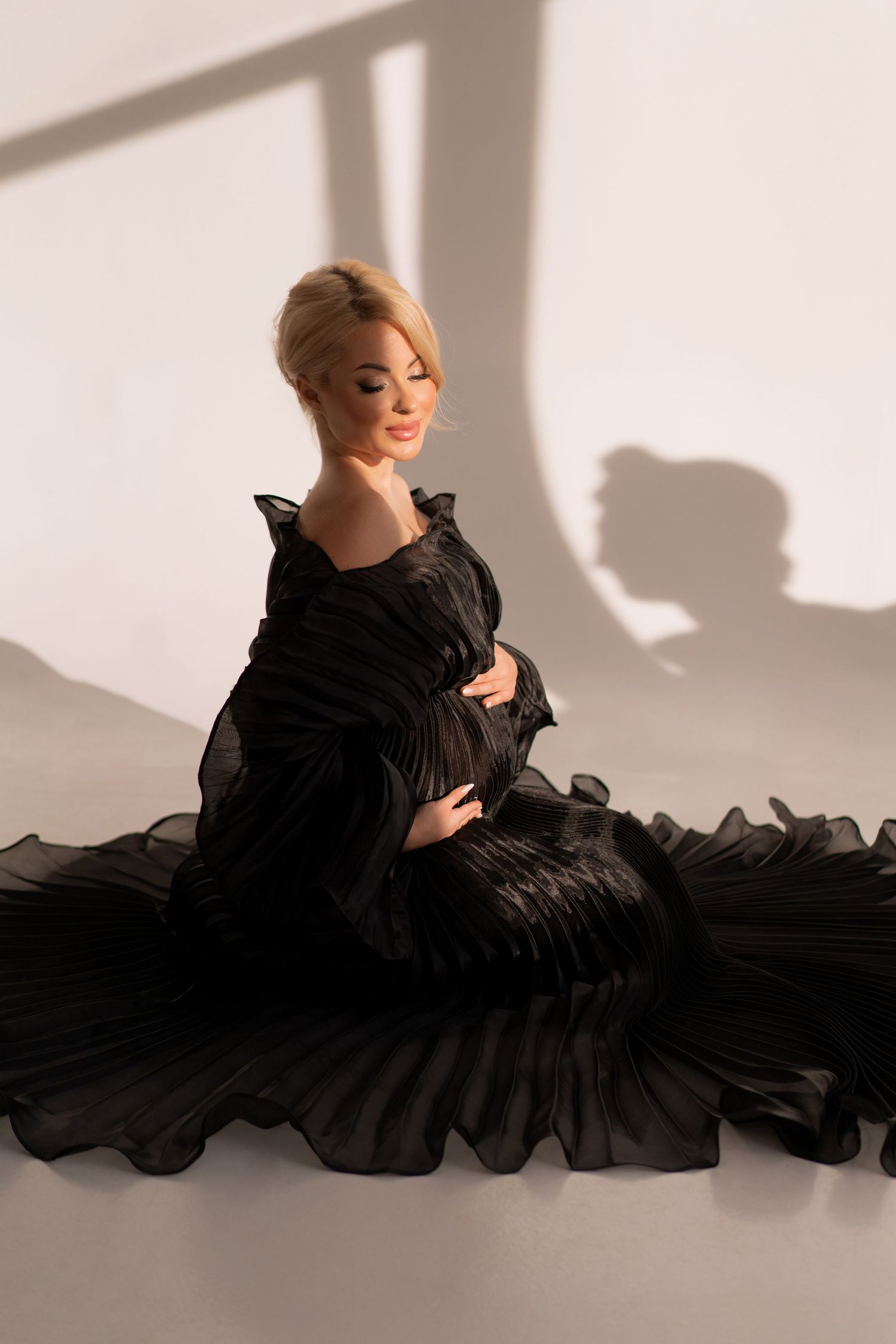 Pregnant blond woman in a professional Chicago studio wearing a ruffled long evening dress posing during maternity photoshoot.