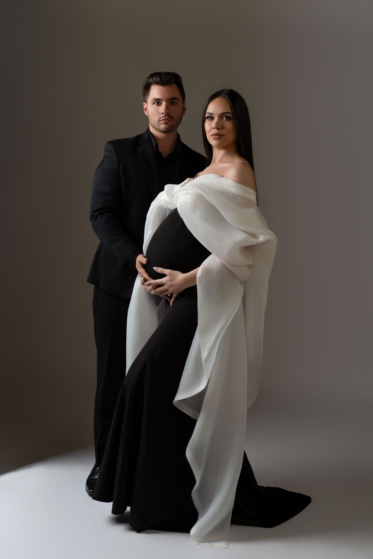 Luxury couple in formal looks posing during their maternity photoshoot in Chicago; the man wearing a suit and the woman in stunning gown.