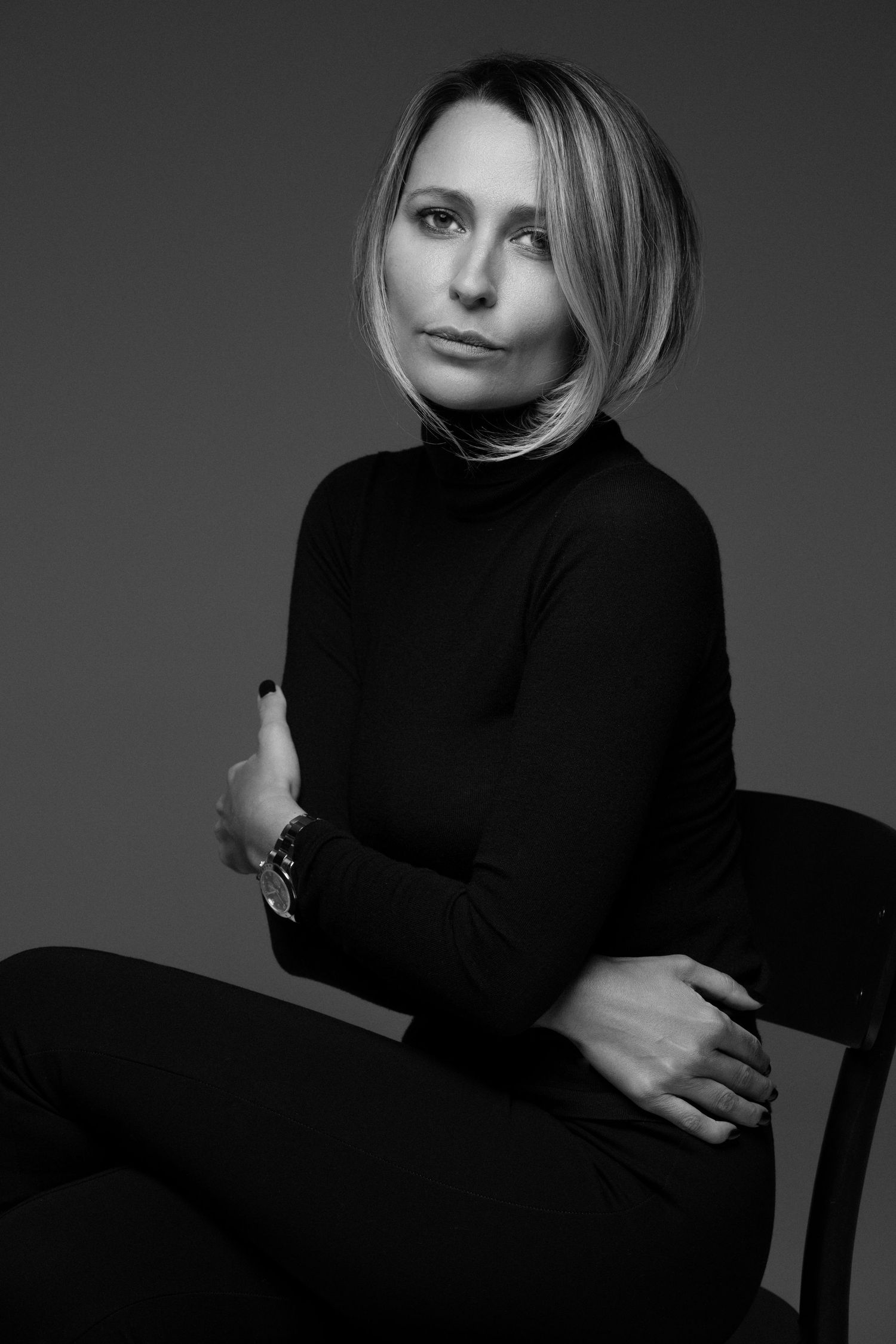 Black and white portrait of a blonde woman in a black sweater sitting on a chair in the studio — minimalist and timeless studio portrait.