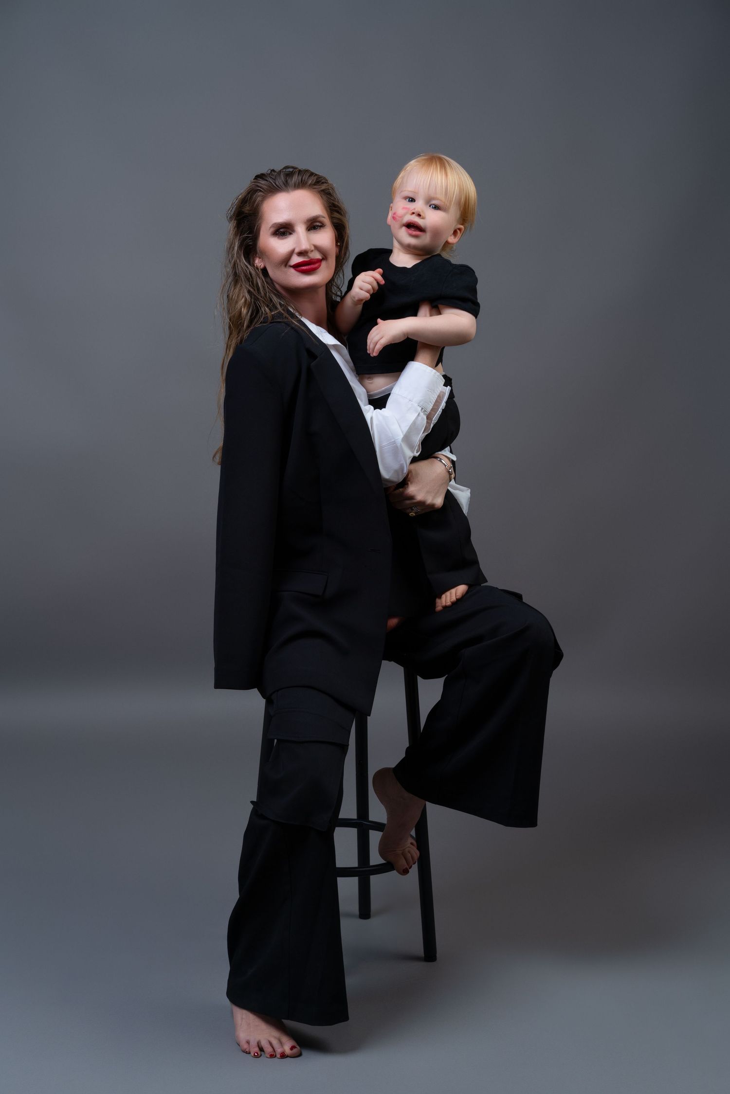 Mommy and Me photoshoot in a Chicago studio featuring a mother wearing a black suit with red lipstick, posing with her child.