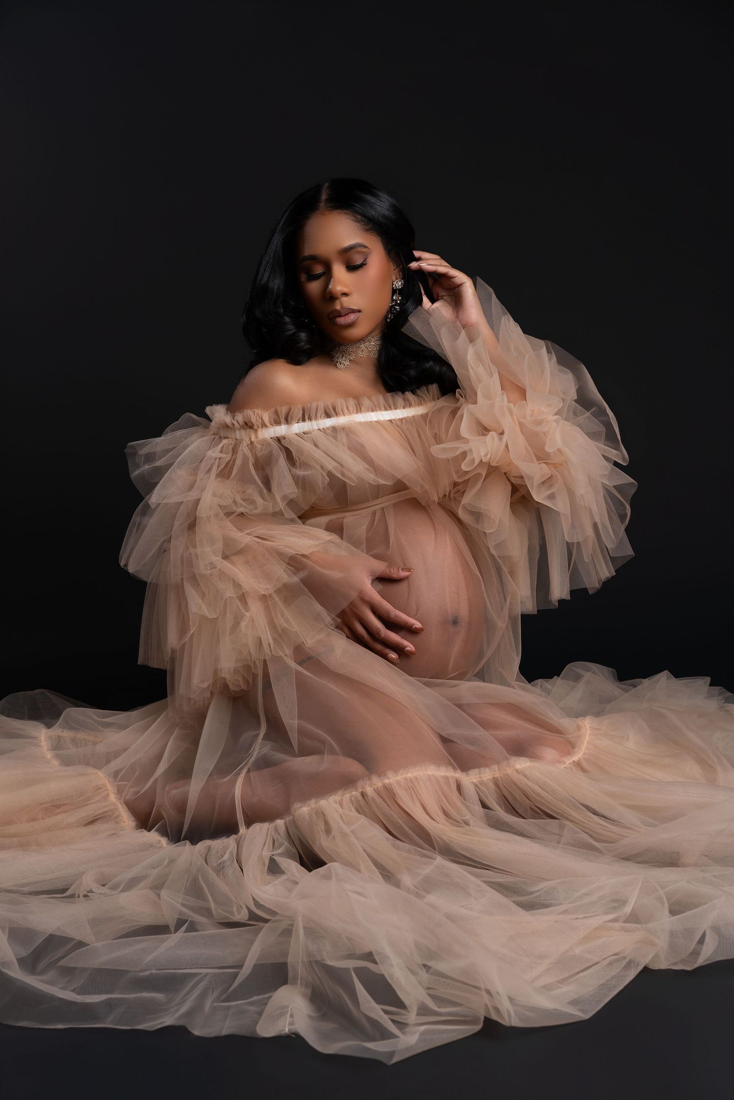 Pregnant woman posing in a beige fluffy dramatic dress during her maternity photoshoot in a Chicago studio.