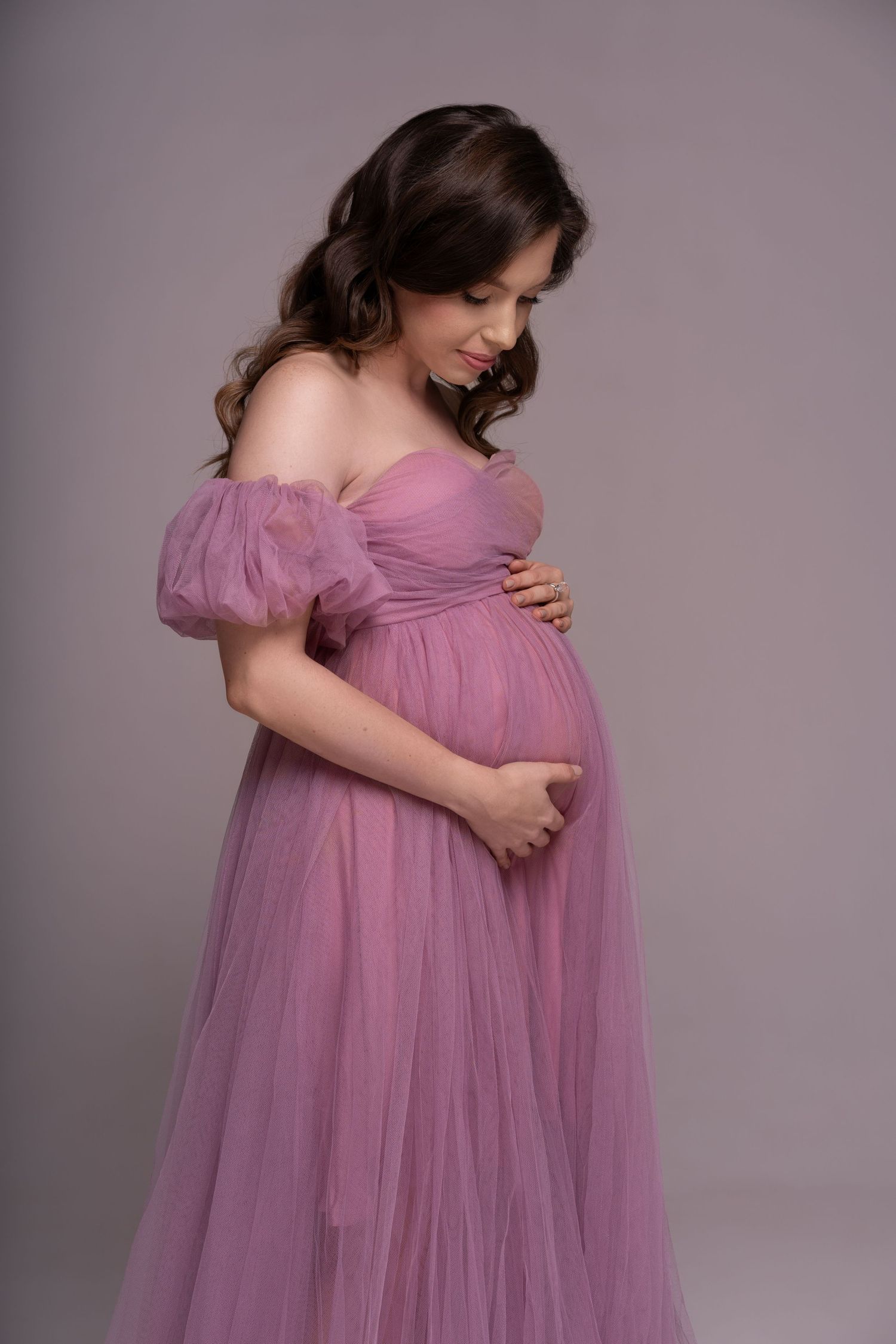 Pregnant women holding hands over the baby bump in a long pink mesh pink dress posing in a studio in Chicago.