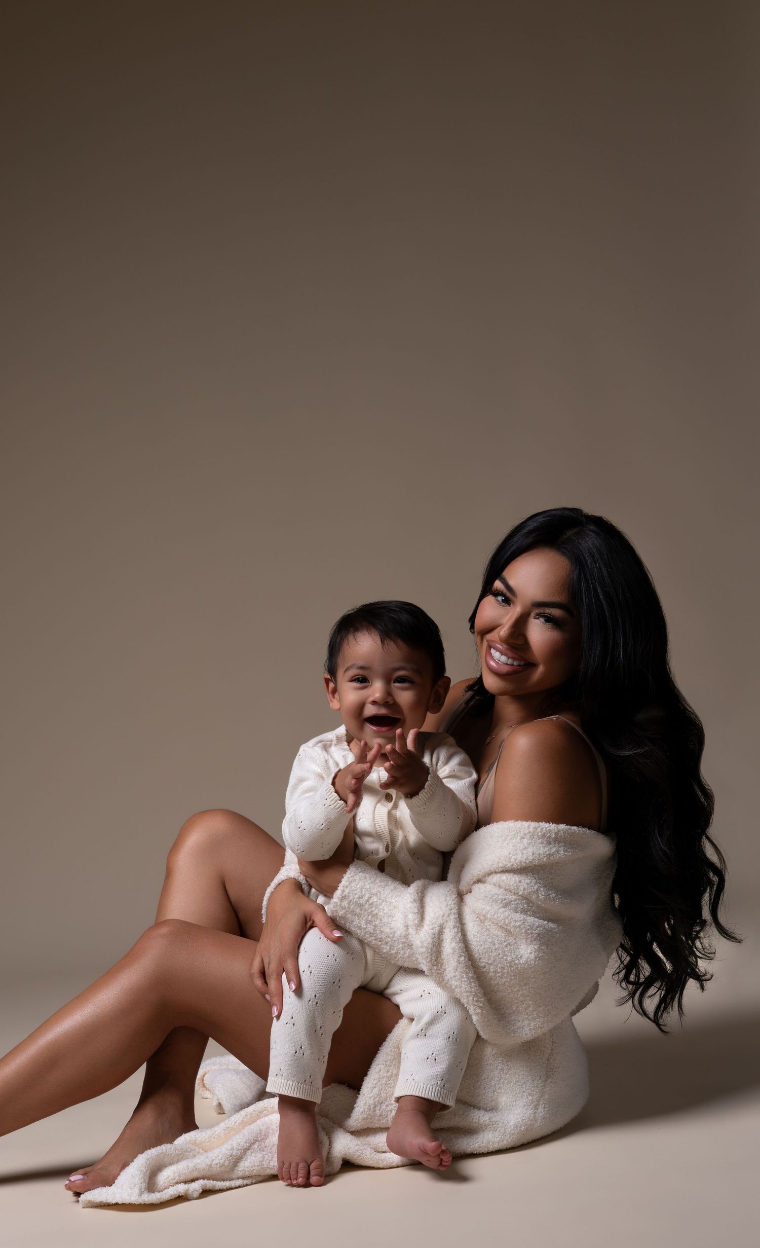 Cozy mommy and me session with mom and son posing on the floor in a Chicago studio. Mother and son in white sweaters.