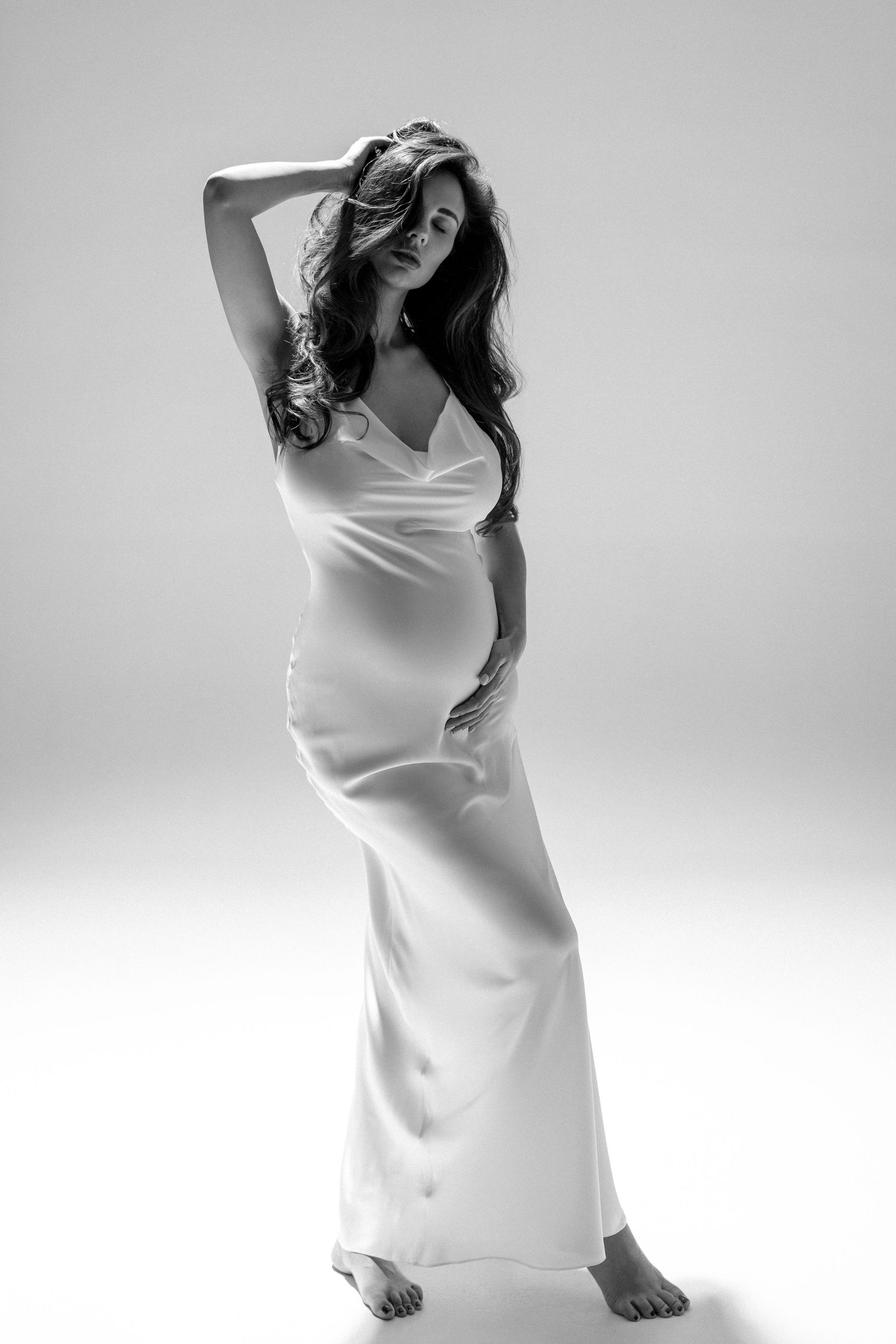 Elegant black and white maternity shot highlighting the curves and beauty of pregnancy, the pregnant women wearing white silk long dress.