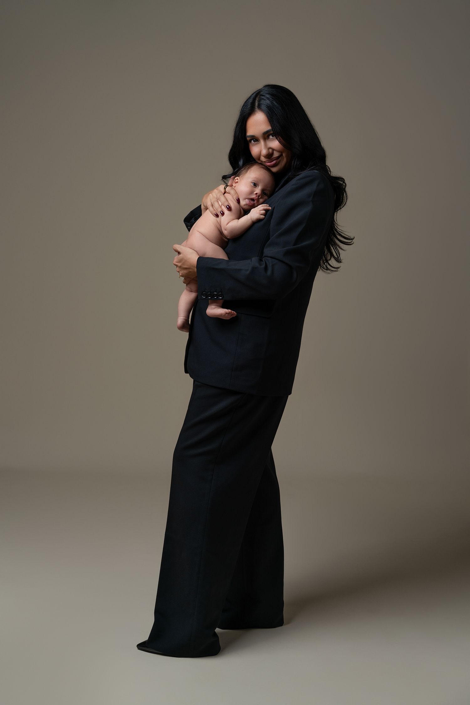 Mommy and Me elegant and luxury newborn photoshoot in a Chicago studio, mother dressed in a black suit gently holding her newborn baby.