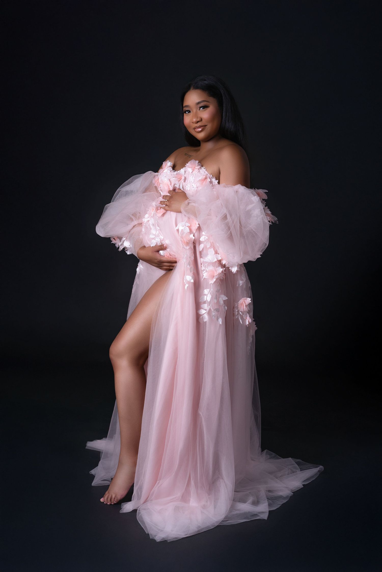 Pregnant woman in a pink long dress with flowers posing during a maternity photoshoot in Chicago. Her hair is dark.