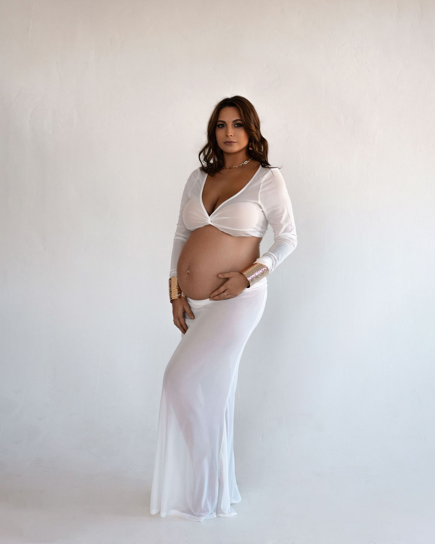 Elegant maternity portrait of a woman in a white gown, embracing her baby bump.