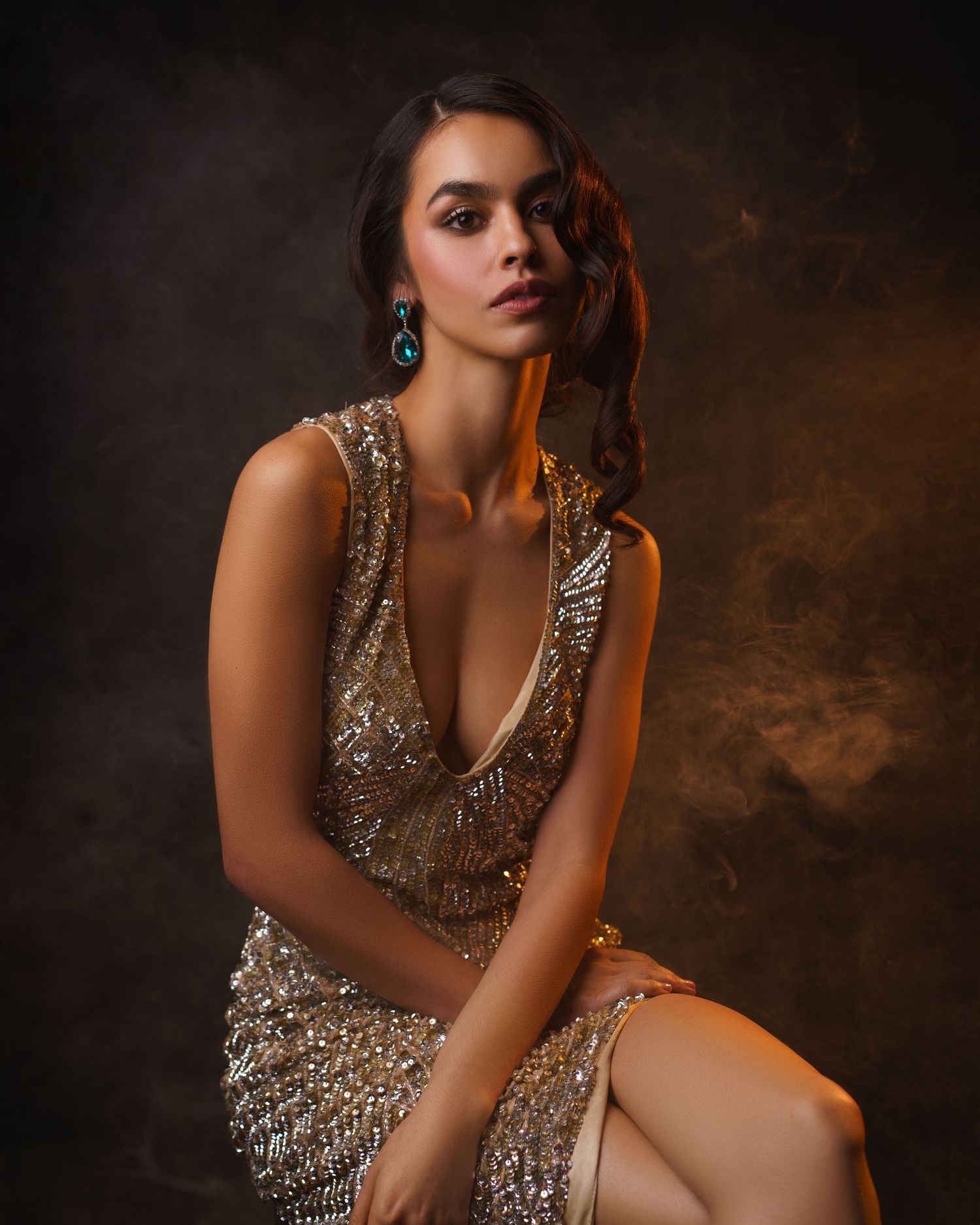 Young woman in a gold dress with blue crystal earrings, evening makeup and hairstyle, posing gracefully — luxury studio portrait in Chicago.