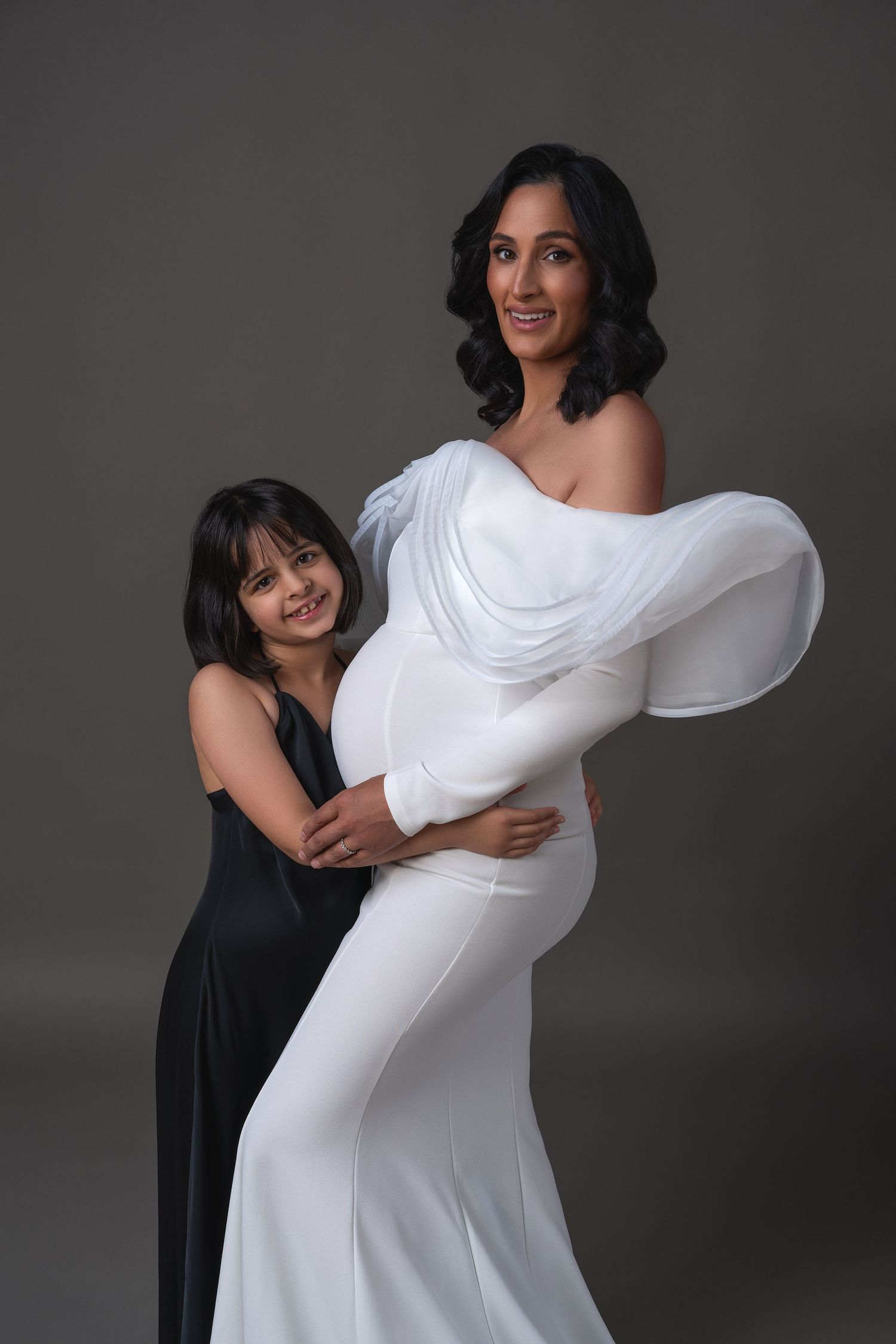 Mommy and daughter maternity session in a professional studio in Chicago. Mother in a white evening dress, daughter in black dress.