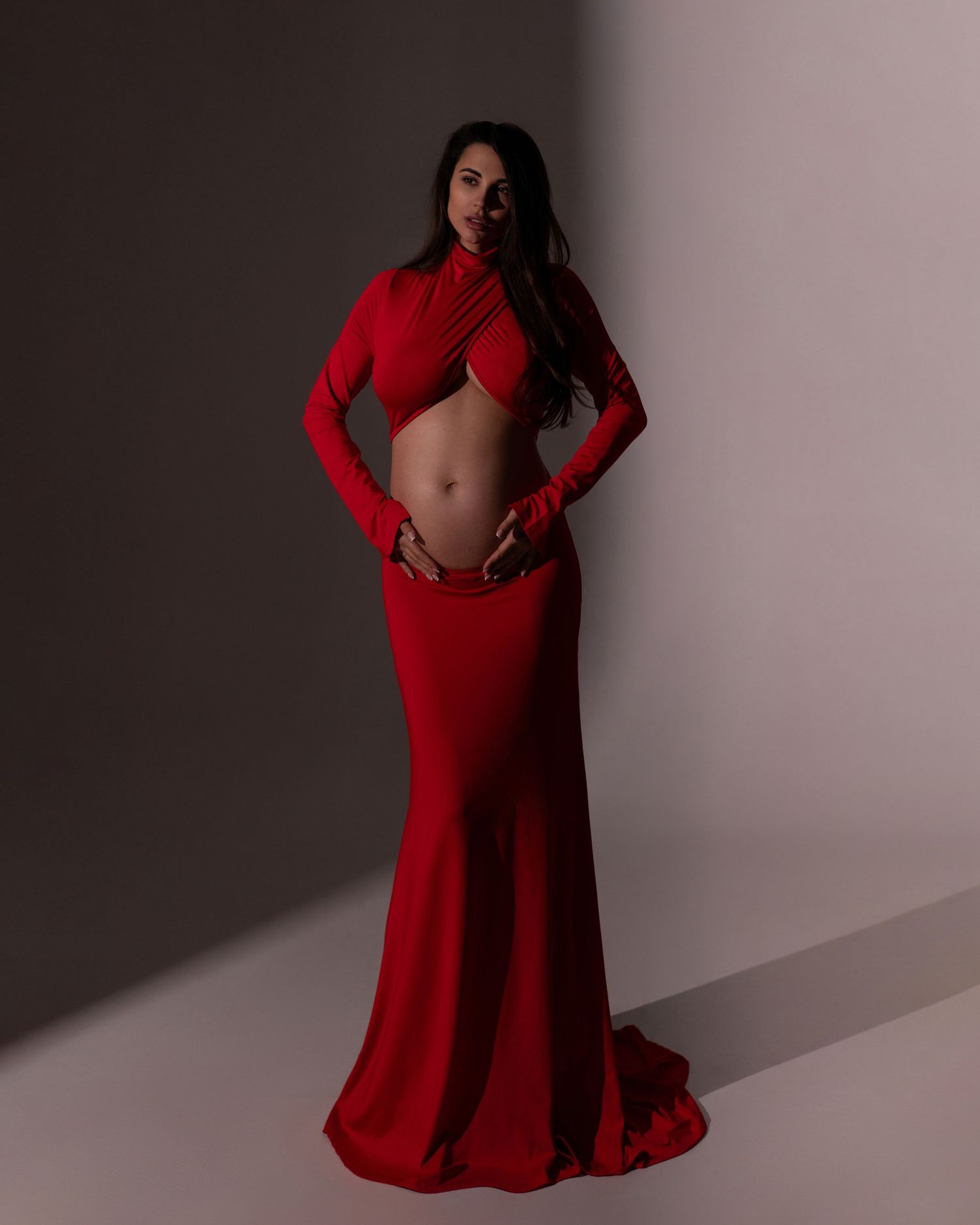 Maternity portrait of a stylish expecting mother in a long red dress posing with confidence and grace.