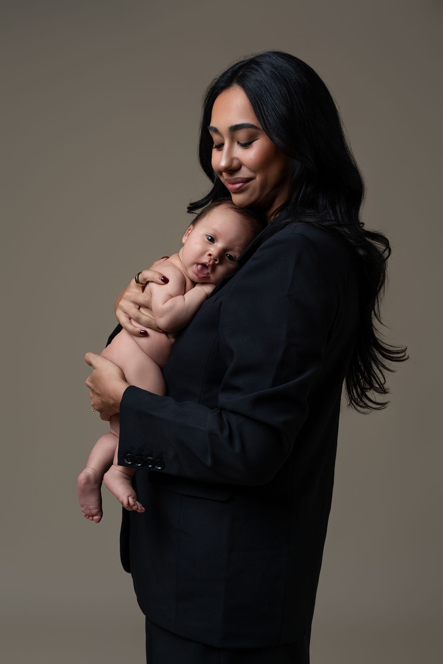 Emotional Mommy and Me newborn portrait in Chicago featuring a mother in a black suit embracing her newborn baby during a tender studio se